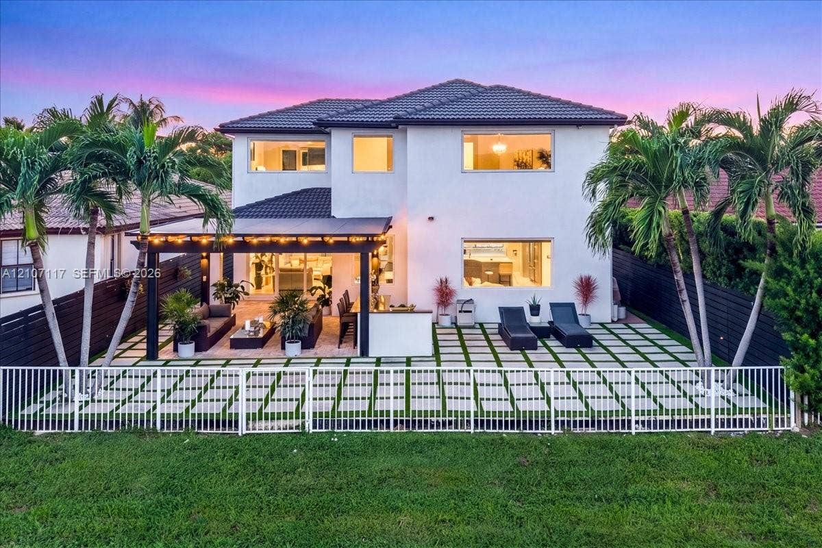7863 NW 111th Court, Doral, FL 33178 Two-story residence featuring a paved patio with turf grid patterns, a covered pergola, integrated outdoor cabinetry, and privacy fencing