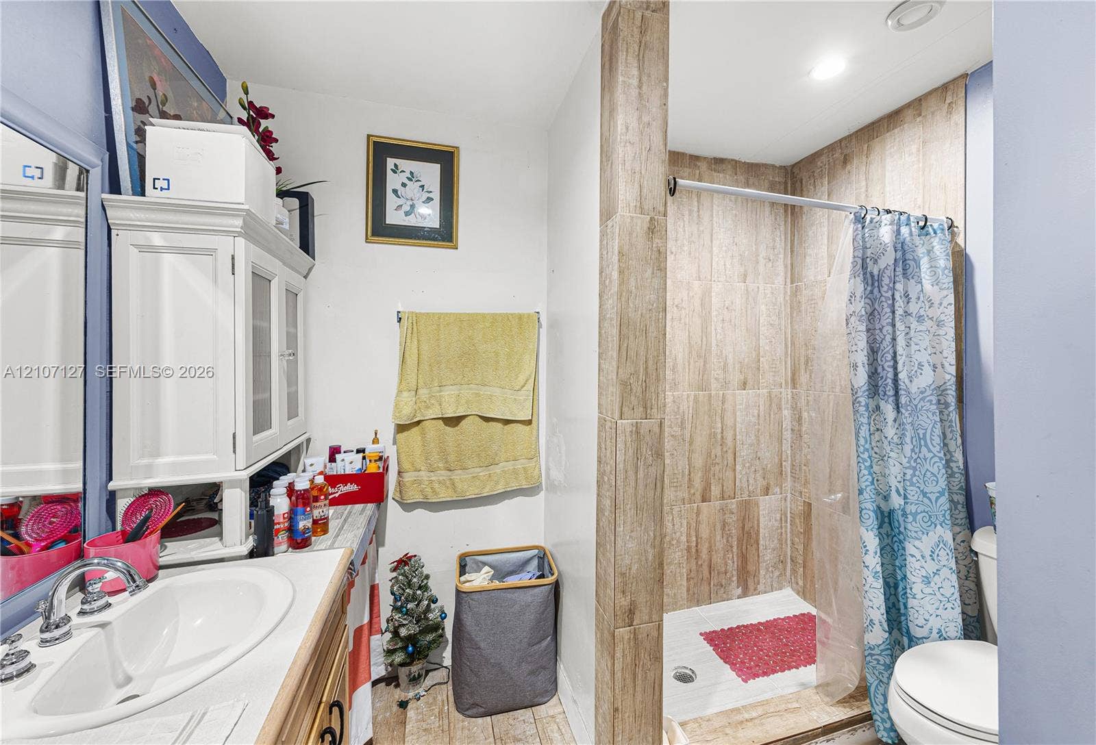Bathroom featuring a shower stall with stone-finish tile surround and a vanity with a white basin and integrated storage cabinet