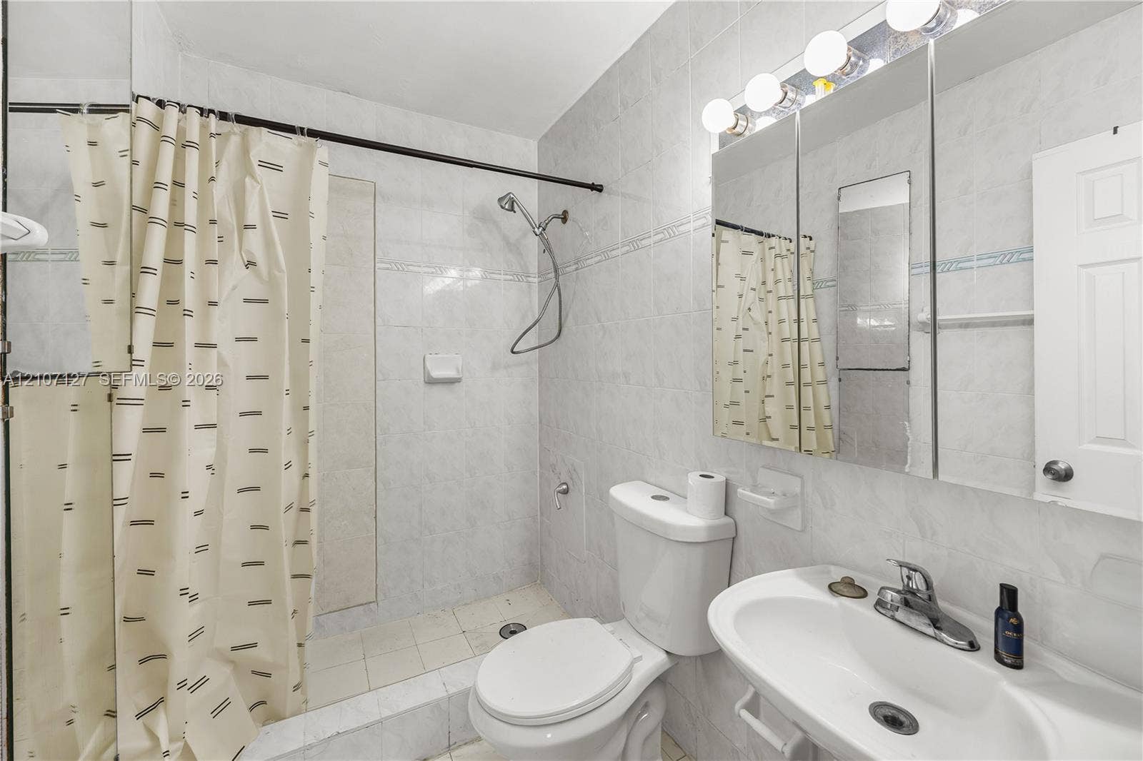 Full bathroom featuring floor-to-ceiling tile, a walk-in shower with a handheld fixture, an integrated medicine cabinet mirror, and a wall-mounted vanity sink with a multi-bulb light fixture