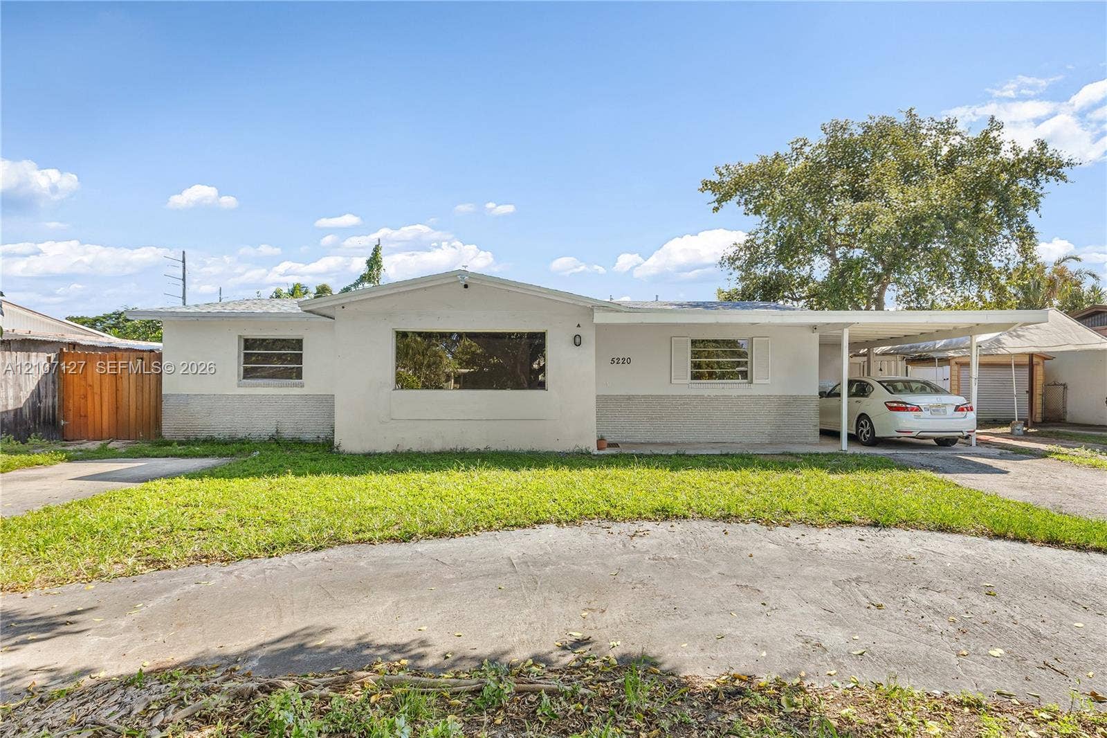 Single-story residence featuring a smooth stucco exterior, a wide front window, a concrete driveway, and an attached carport