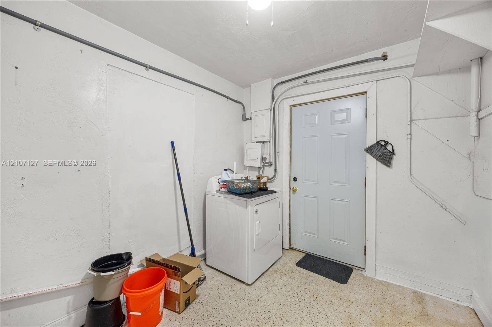 Utility space featuring smooth wall finishes, overhead lighting, and a six-panel exterior access door