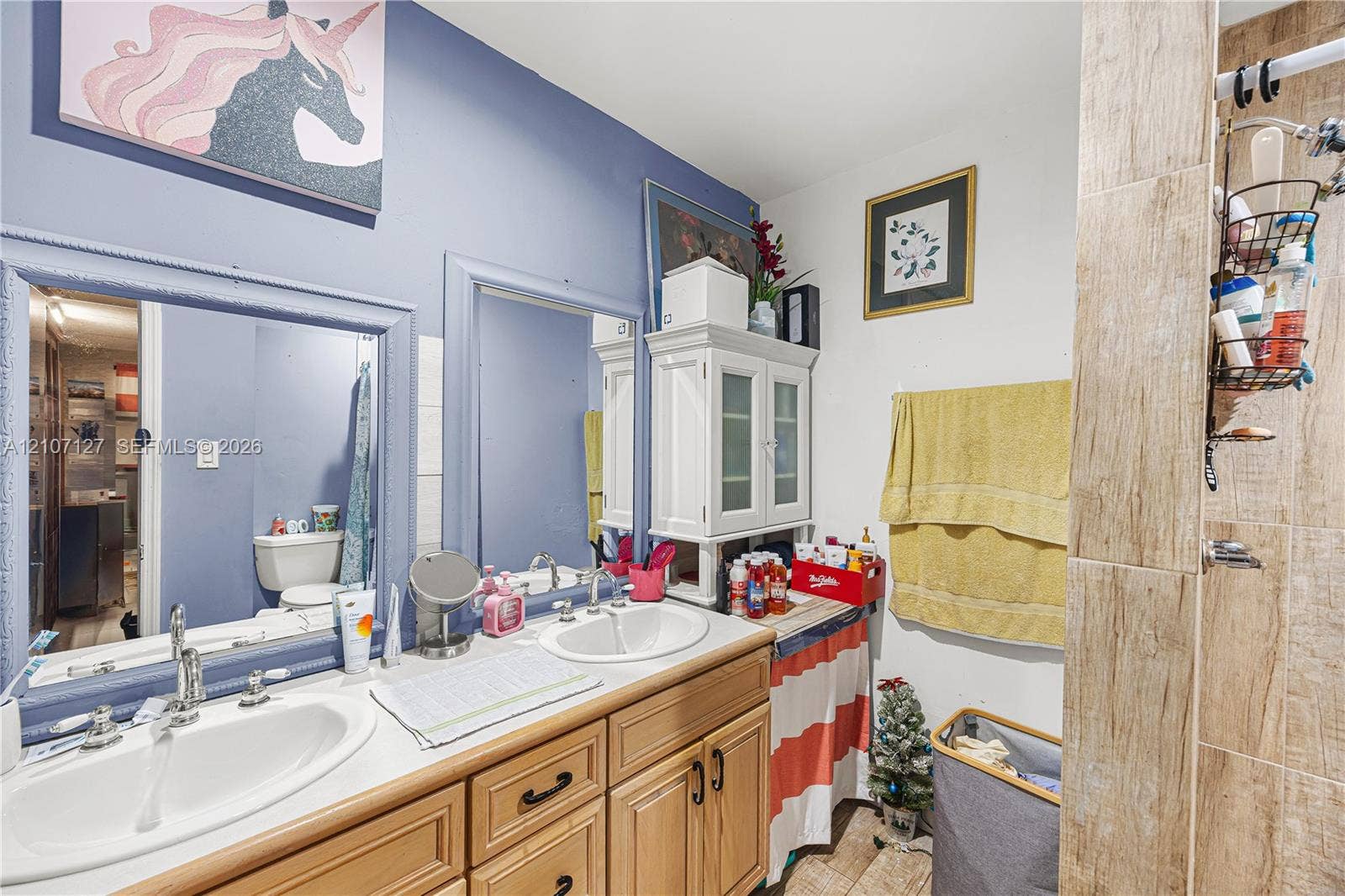 Double vanity featuring inset sinks, wood-finish cabinetry, framed mirrors, and a wall-mounted glass-door cabinet