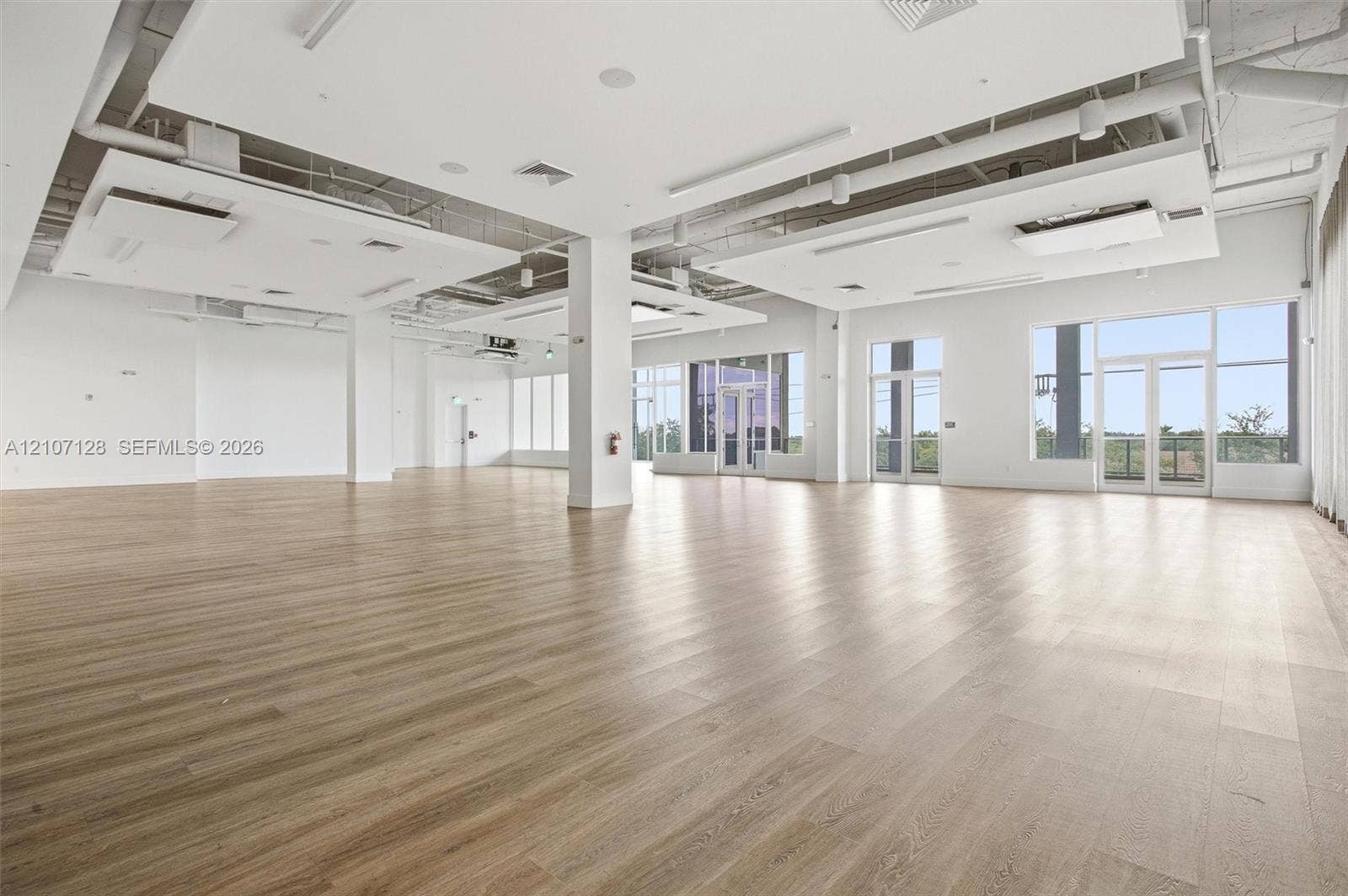 7875 NW 107th Avenue, #802, Doral, Doral, FL 33178 Expansive open-concept interior featuring wood-finish flooring, suspended ceiling architectural panels, structural columns, and floor-to-ceiling windows with glass-panel doors