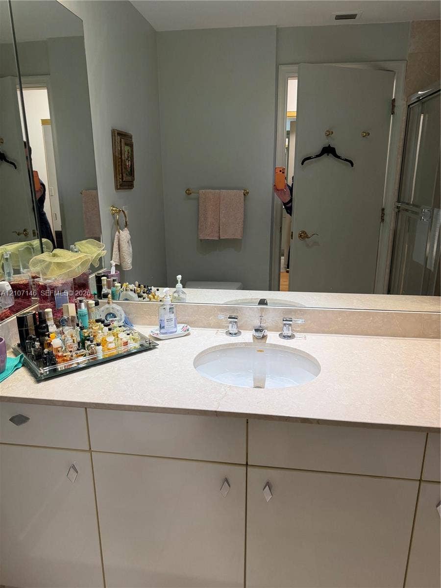 Bathroom vanity featuring a light-toned countertop, integrated oval basin, polished chrome widespread faucet, and flat-panel cabinetry
