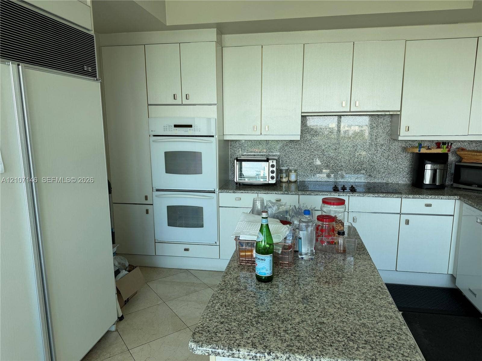 Kitchen featuring white cabinetry, stone countertops, stone backsplash, integrated double oven, and integrated refrigerator