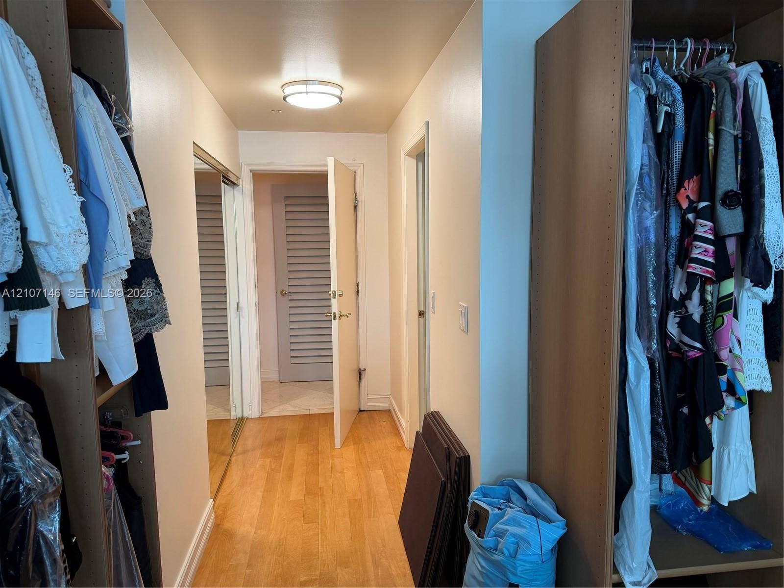 Walk-in closet featuring floor-to-ceiling built-in wood cabinetry, wood-finish flooring, mirrored sliding doors, and flush-mount ceiling lighting