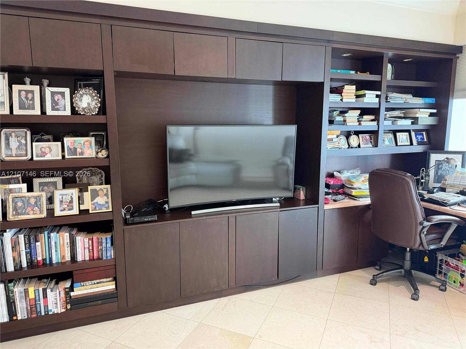 Floor-to-ceiling dark wood built-in cabinetry featuring extensive open shelving, integrated desk surface, recessed task lighting, and central media enclosure