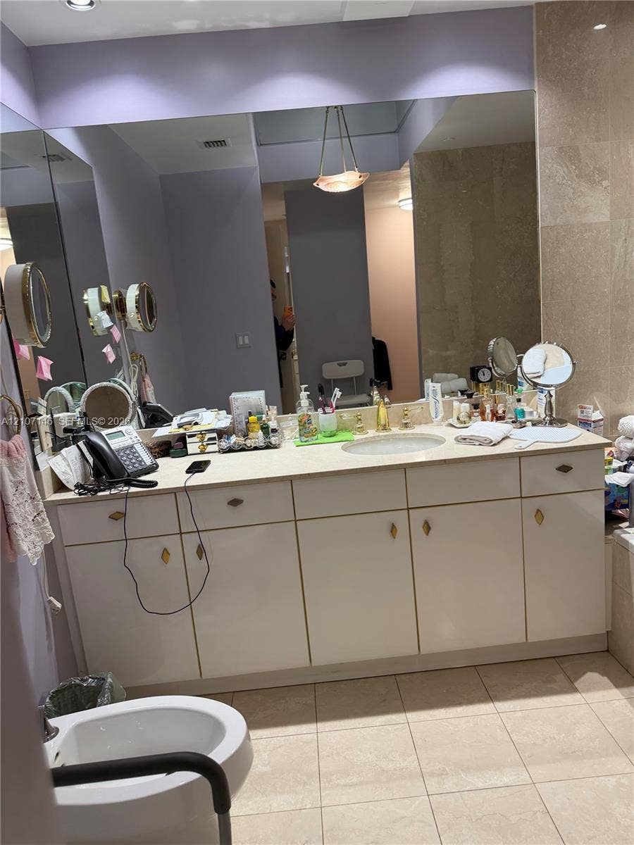 Bathroom vanity featuring a light-toned countertop, integrated oval sink, extensive white cabinetry, large wall-mounted mirror, and tile flooring
