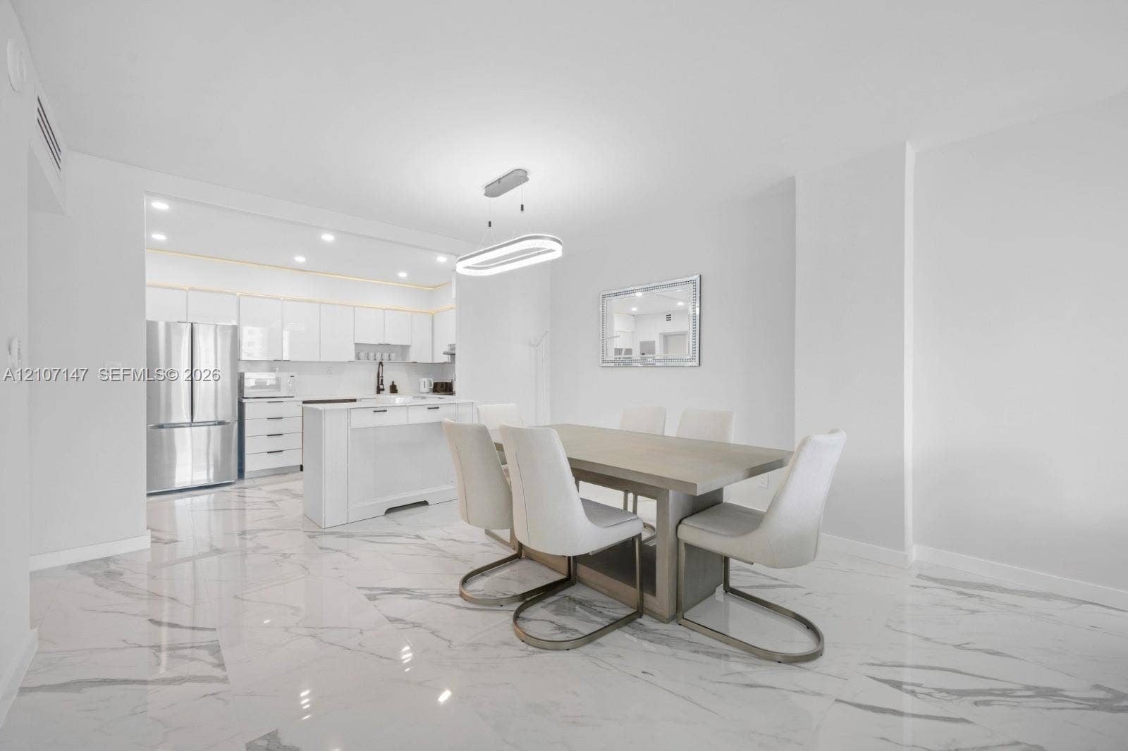 Polished stone-finish flooring, kitchen island with built-in cabinetry, stainless steel refrigerator, and modern oval-shaped pendant lighting