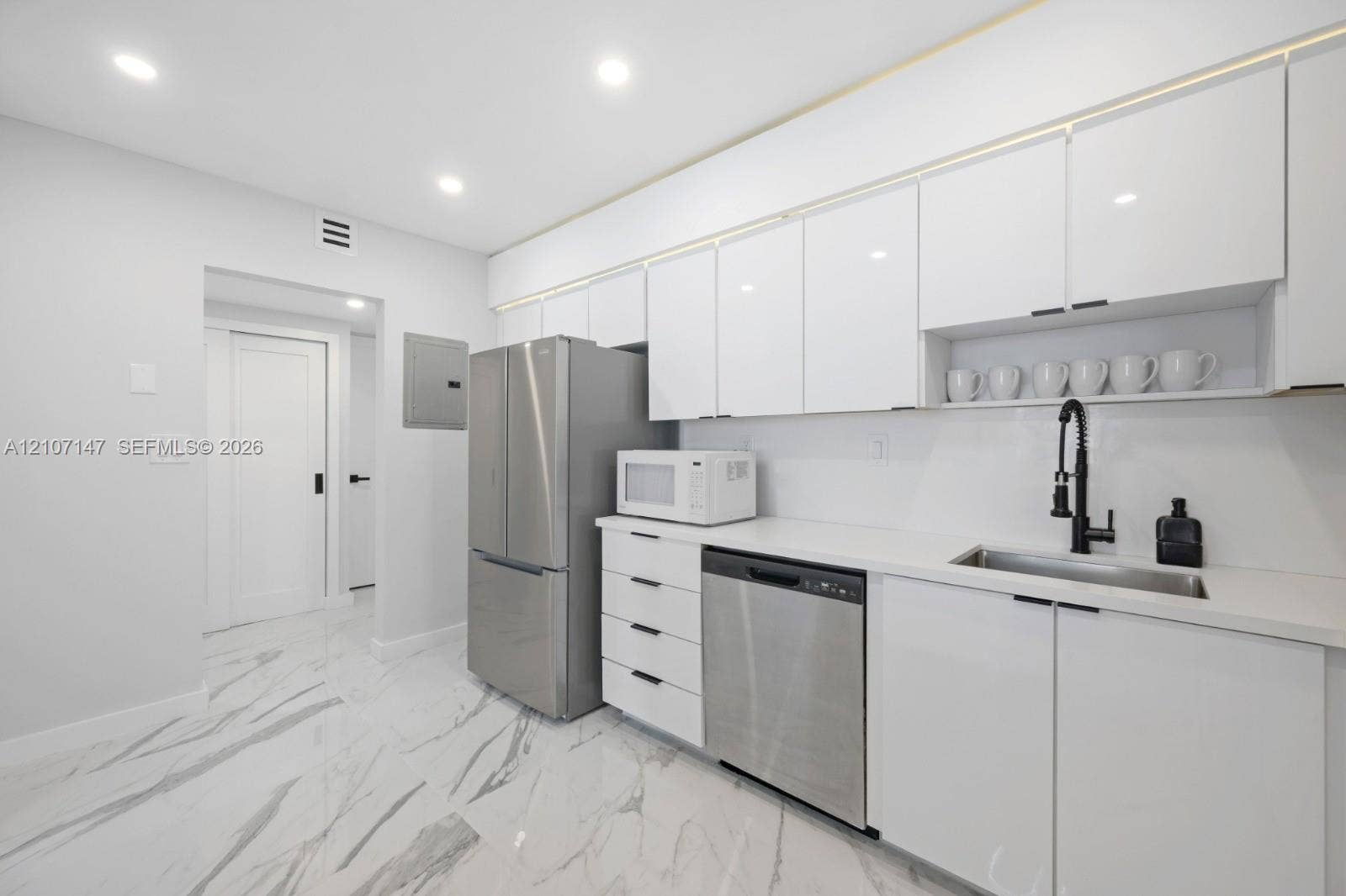 Kitchen featuring white high-gloss cabinetry, stainless steel appliances, solid-surface countertops, a matte black pull-down faucet, and polished stone-finish tile flooring