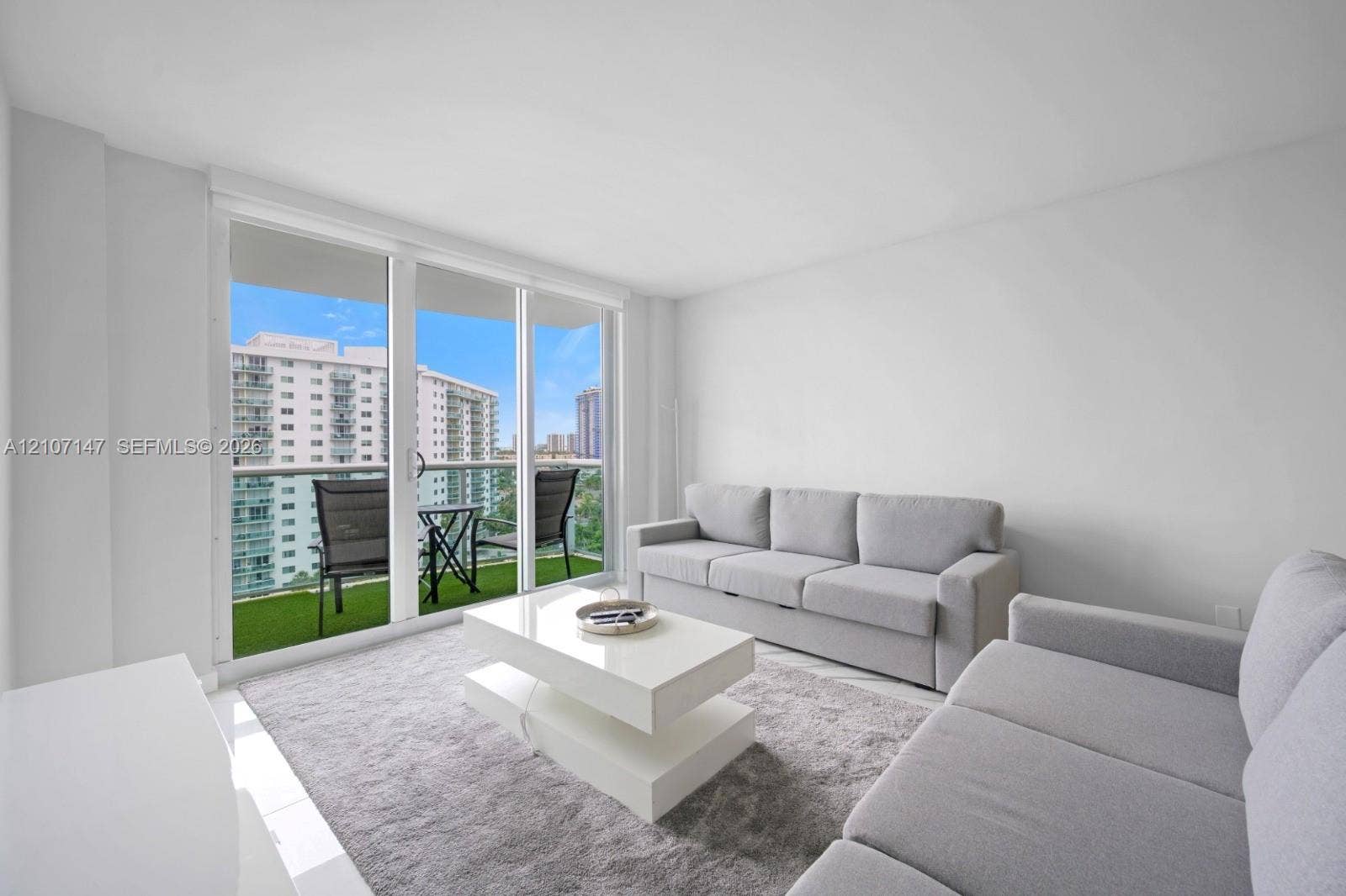 Floor-to-ceiling sliding glass door, private balcony with synthetic grass flooring, and white-finish walls