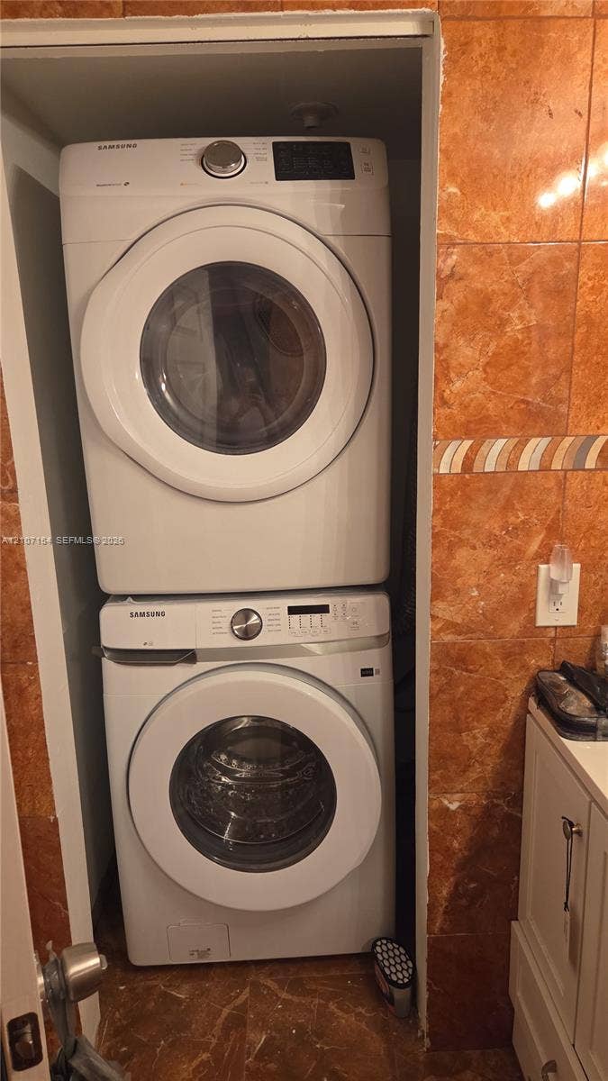 450 Commodore Drive, #311, Plantation, FL 33325 Stacked front-loading washer and dryer unit, set within a dedicated recessed laundry alcove featuring tile wall finishes and decorative border accents