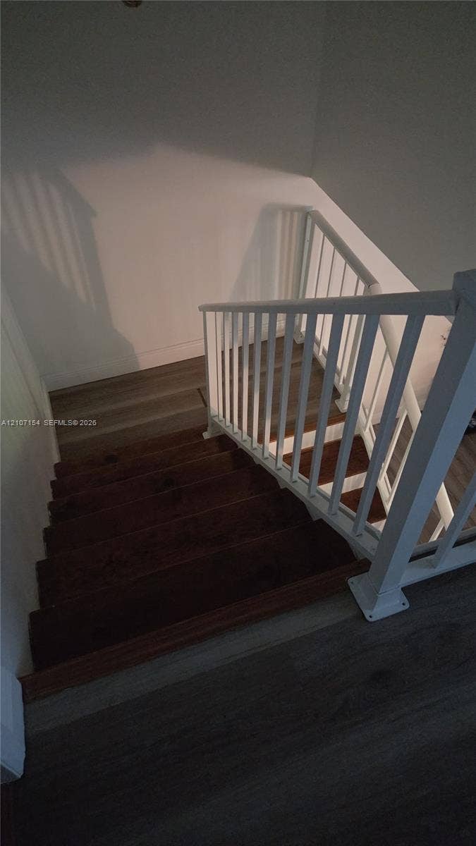 450 Commodore Drive, #311, Plantation, FL 33325 Staircase featuring dark-stained wooden treads, white railing with vertical balusters, and grey wood-finish flooring