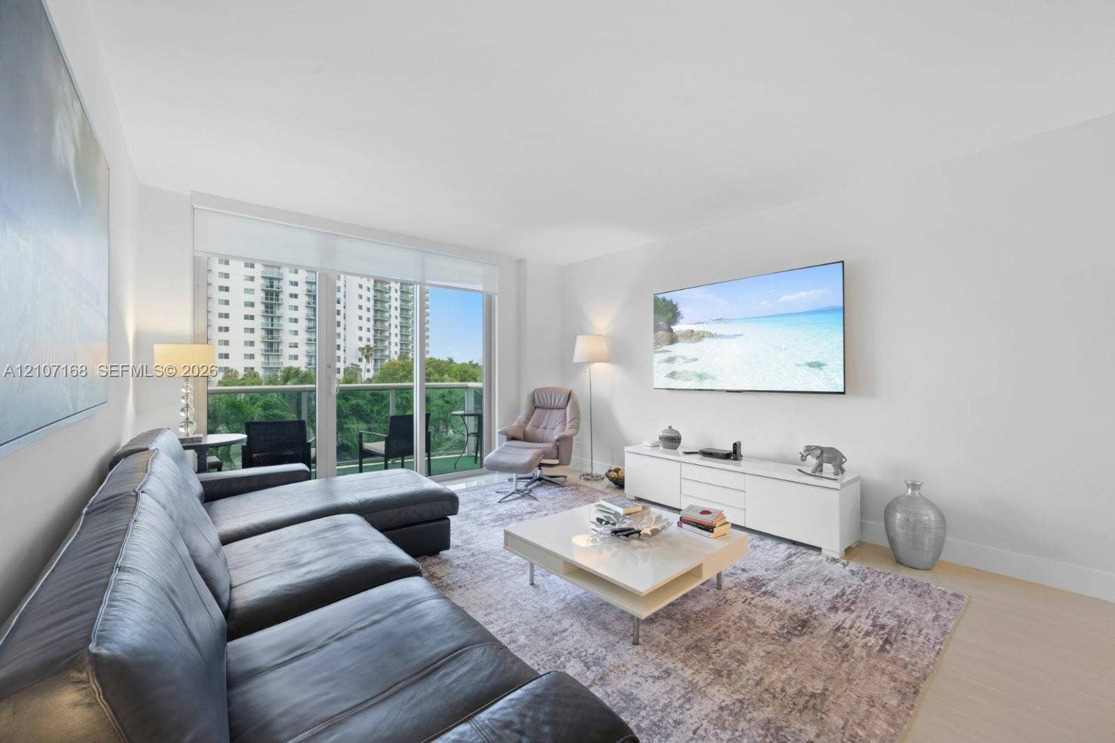 Living area featuring floor-to-ceiling glass sliding doors, private balcony access, and light-toned wood-finish flooring
