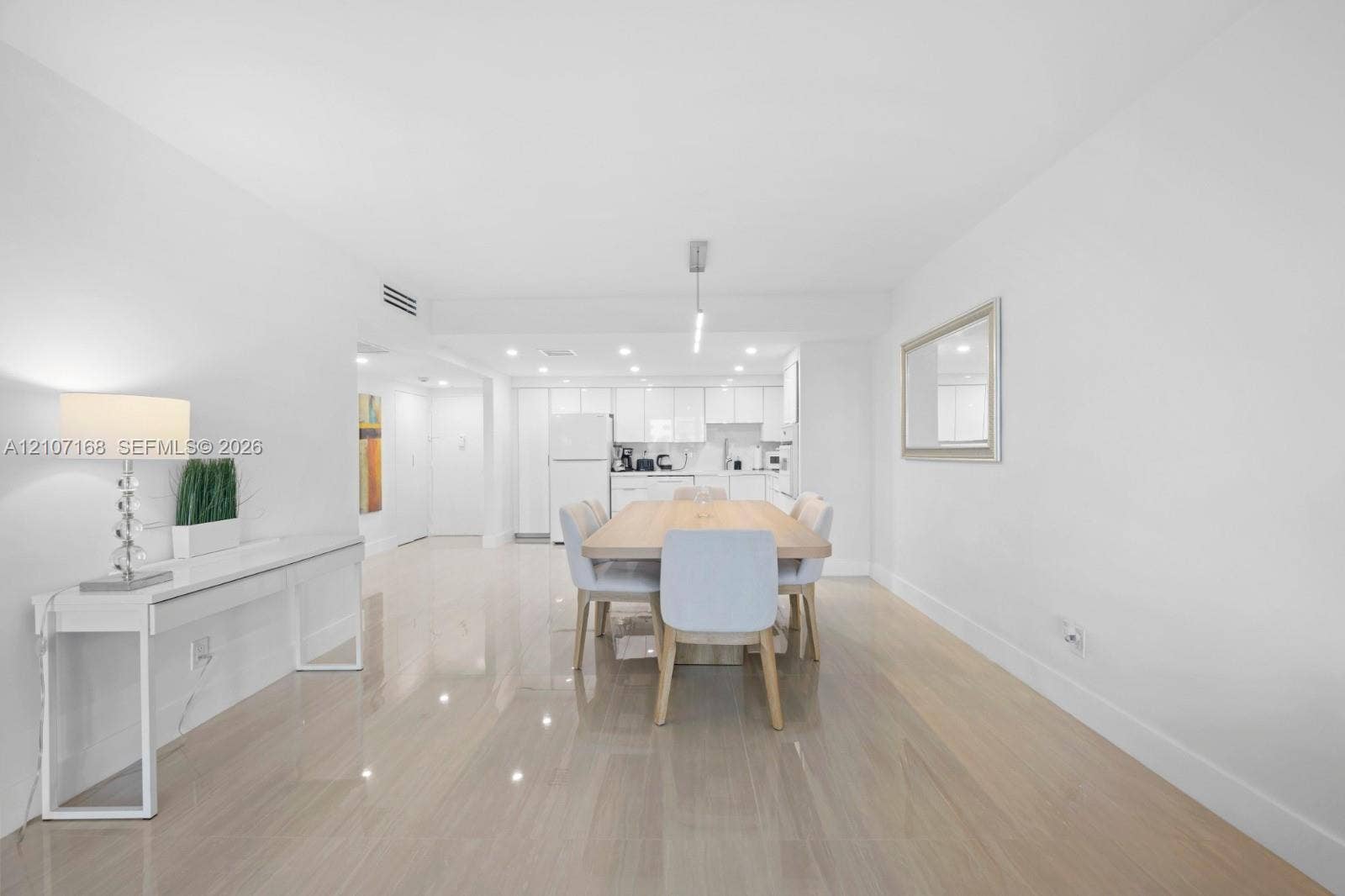 Open-concept interior featuring light-toned wood-finish flooring, high-gloss white cabinetry, recessed ceiling lighting, and a linear pendant light fixture