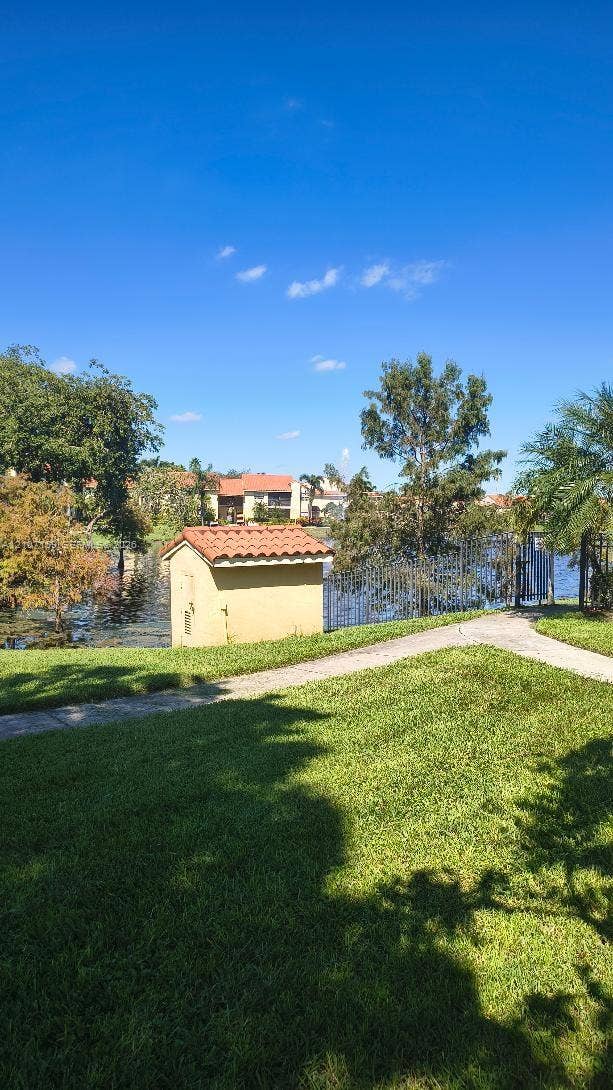 1267 SW 46th Avenue, #2311, Pompano Beach, Pompano Beach, FL 33069 Expansive lawn area featuring paved walkways, a utility structure with a red tile roof, and waterfront perimeter fencing