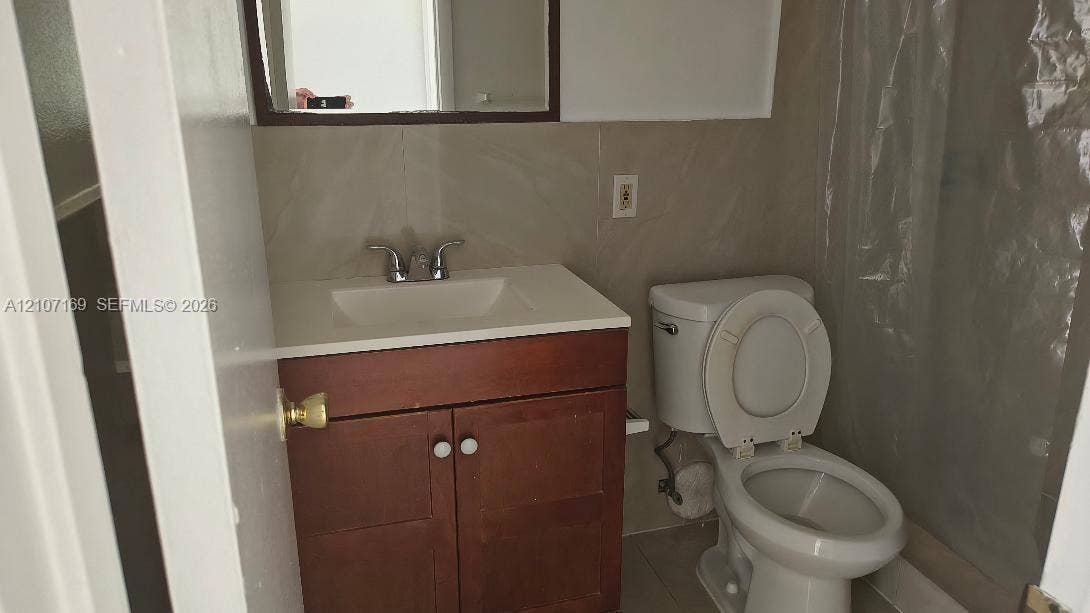 1267 SW 46th Avenue, #2311, Pompano Beach, Pompano Beach, FL 33069 Wood-finish vanity cabinet, integrated sink with dual-handle faucet, wall-mounted mirror, and tile wall surround