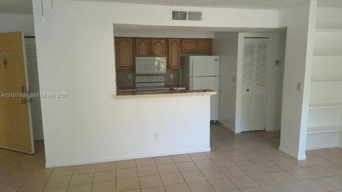 1267 SW 46th Avenue, #2311, Pompano Beach, Pompano Beach, FL 33069 Kitchen featuring wood cabinetry, white appliances, a breakfast bar, tiled flooring, and built-in shelving