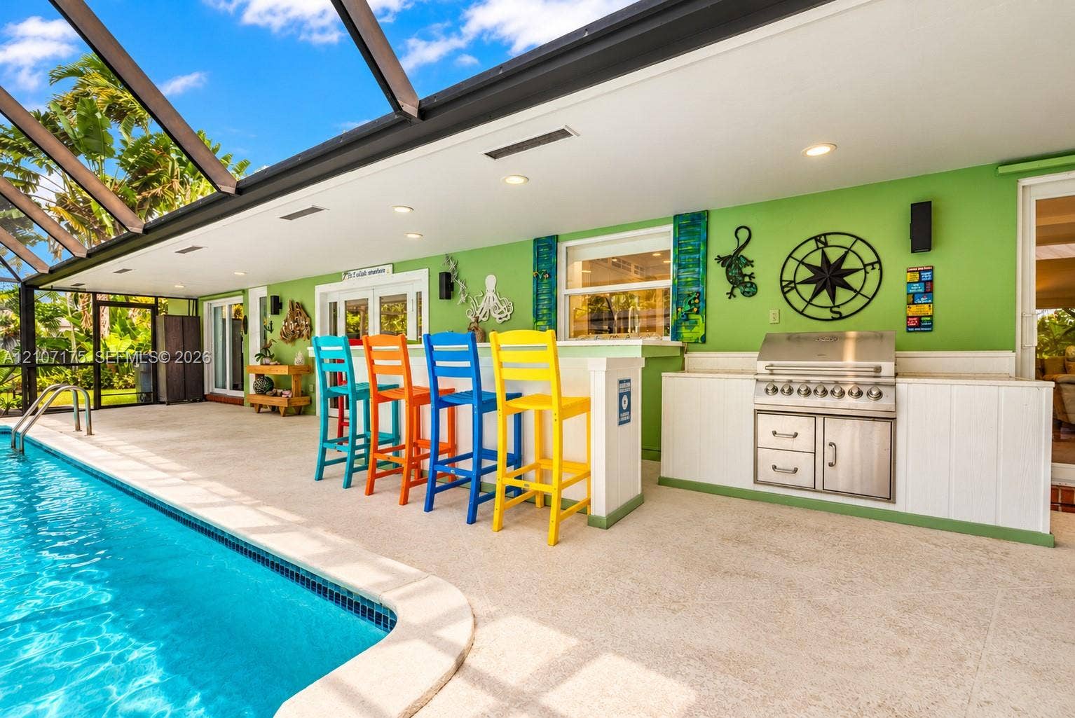 17550 SW 86th Avenue, Palmetto Bay, FL 33157 Screened lanai featuring a built-in outdoor kitchen with stainless steel grill, composite bar-height counter, recessed ceiling lighting, and pool with aggregate decking
