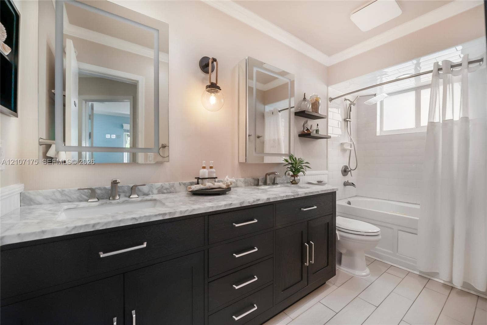 17550 SW 86th Avenue, Palmetto Bay, FL 33157 Hallway Bath. Double vanity featuring dark cabinetry, stone-finish countertops, lighted dual mirrored cabinets, wall-mounted lighting, and a bathtub-shower combination.