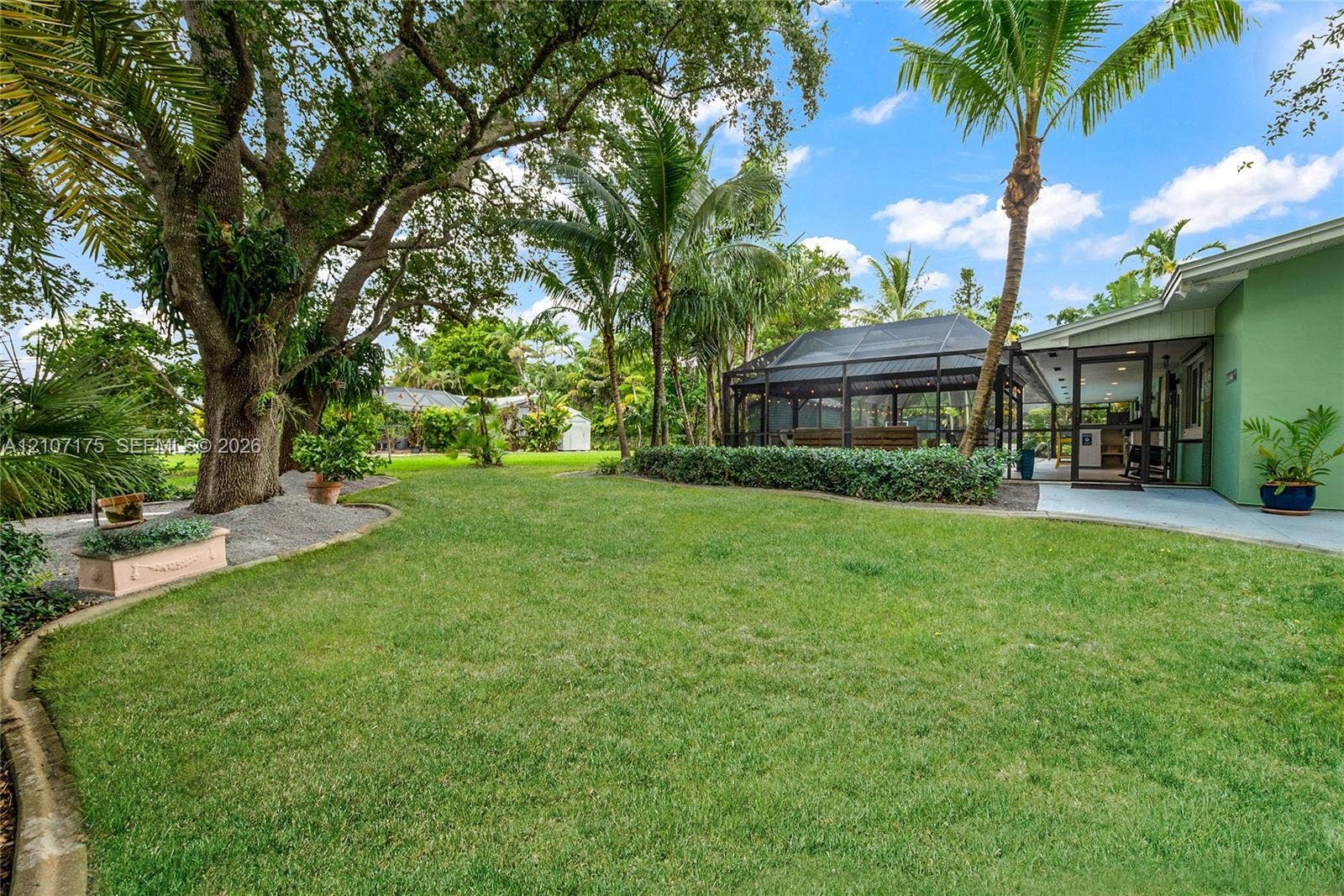 17550 SW 86th Avenue, Palmetto Bay, FL 33157 Expansive backyard featuring a manicured lawn, mature trees, and landscaped garden borders.