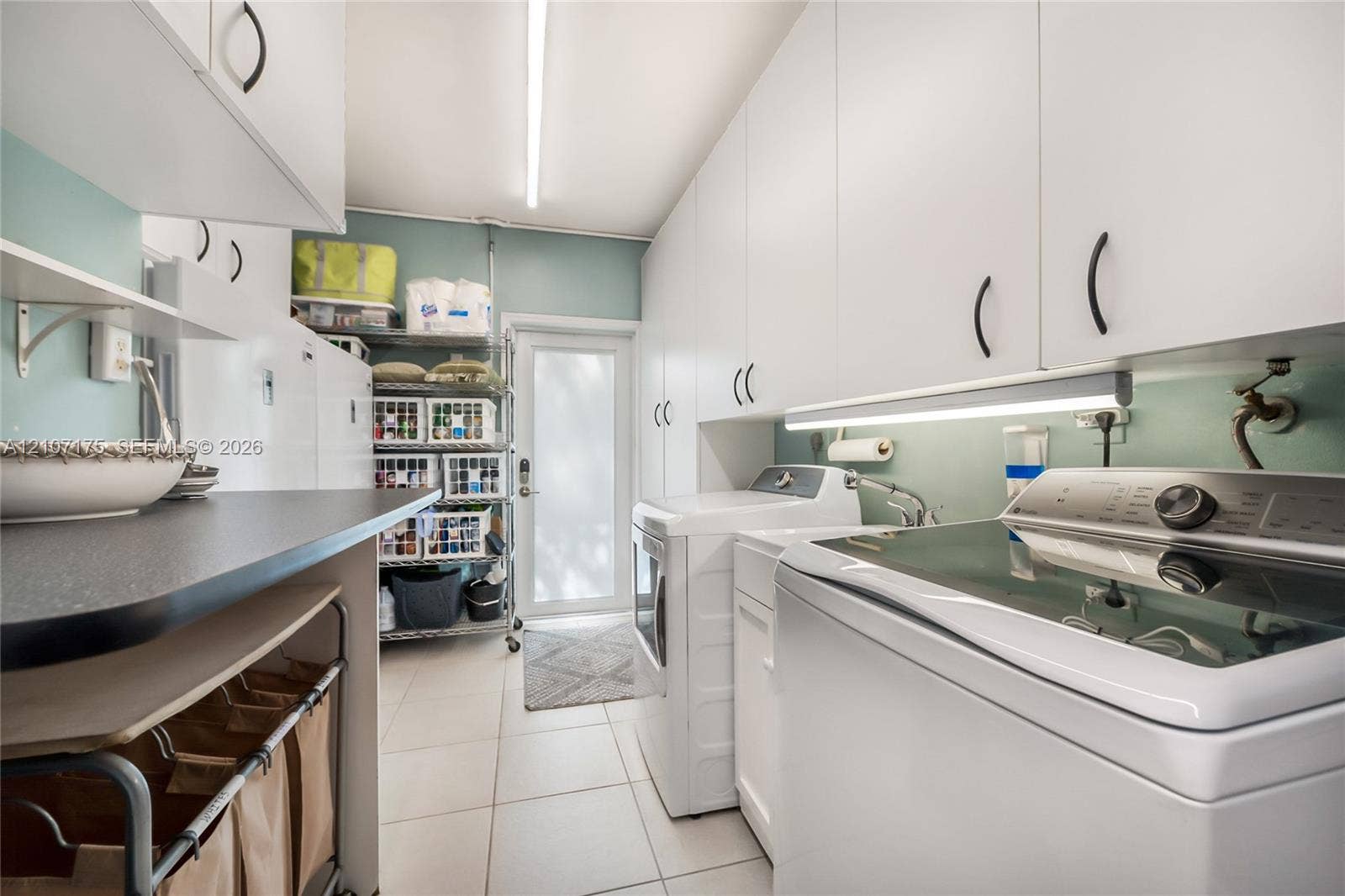 17550 SW 86th Avenue, Palmetto Bay, FL 33157 Laundry room featuring laundry tub, extensive white cabinetry, light-toned tile flooring, under-cabinet lighting, and impact glass exterior door.