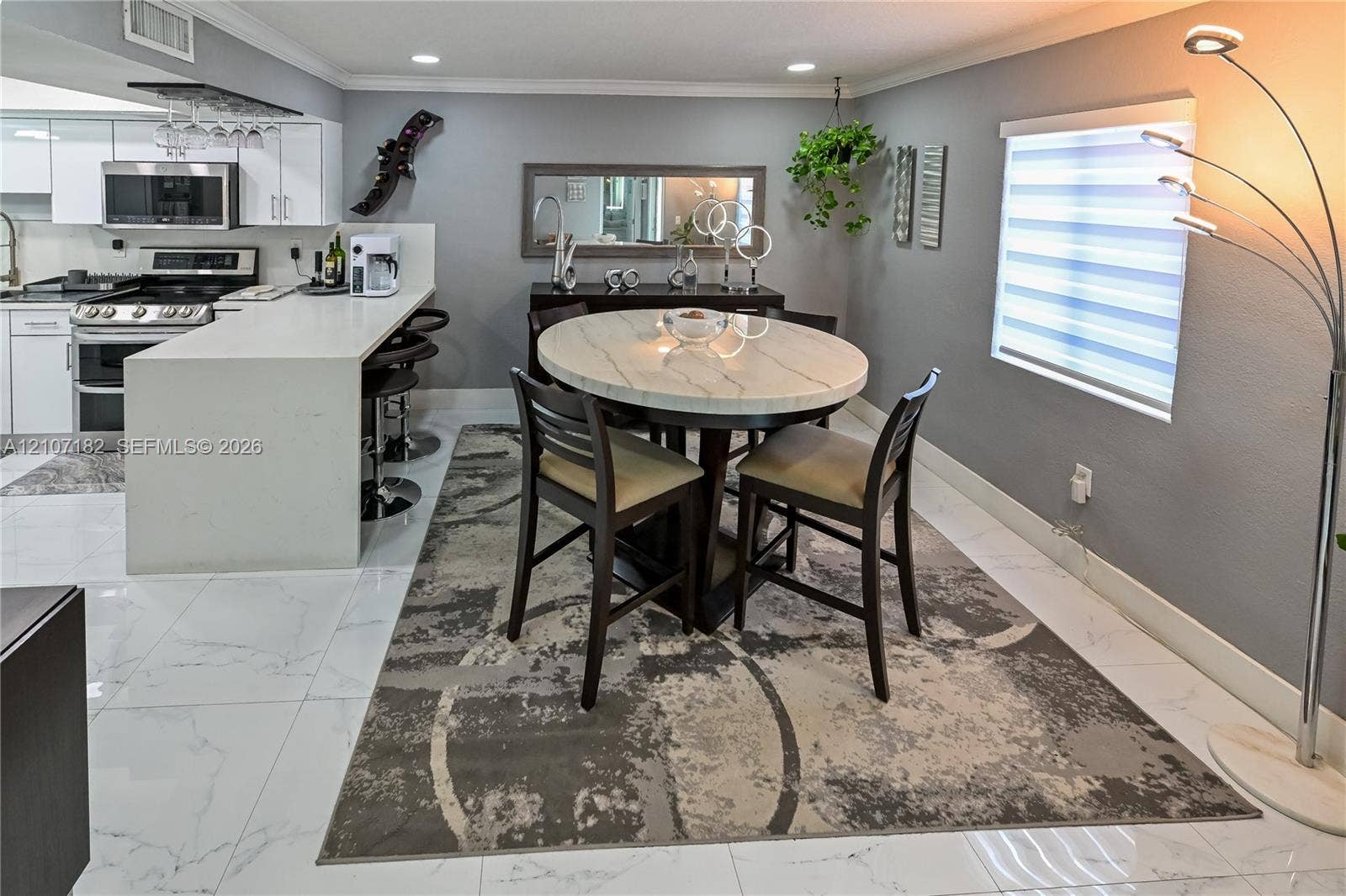 Open-concept kitchen featuring a quartz waterfall island, high-gloss white cabinetry, stainless steel appliances, recessed ceiling lighting, and large-format porcelain tile flooring