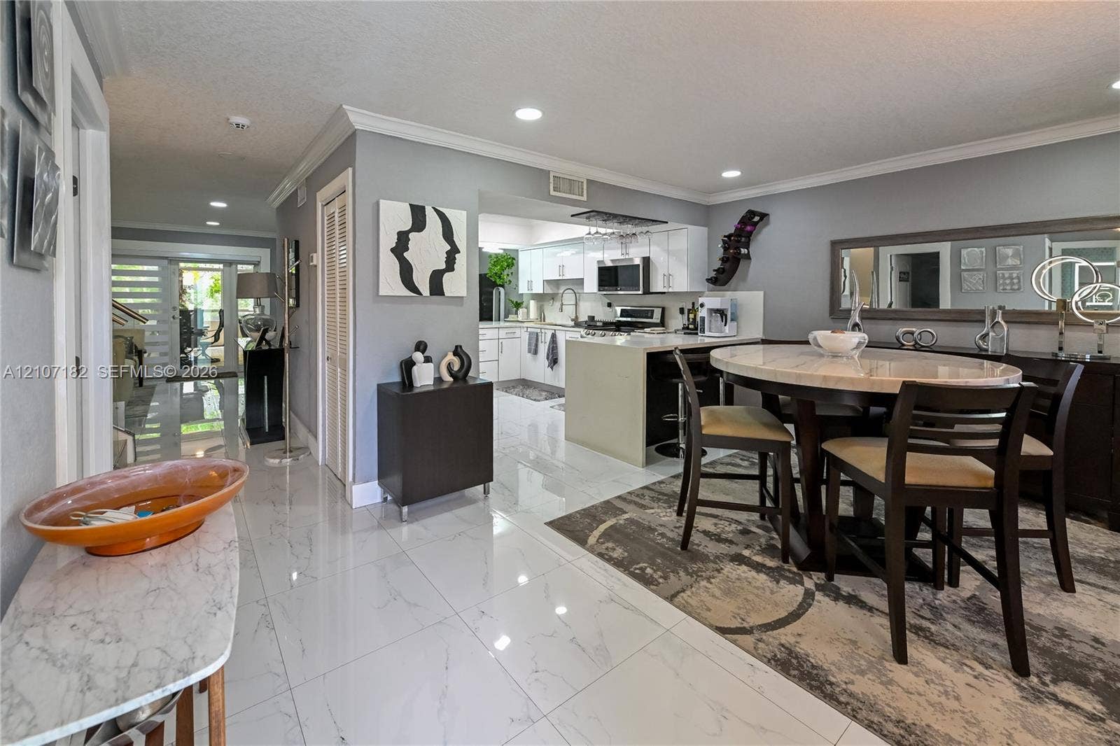 Open-concept interior featuring large-format polished tile flooring, recessed lighting, crown molding, and an island kitchen with white cabinetry