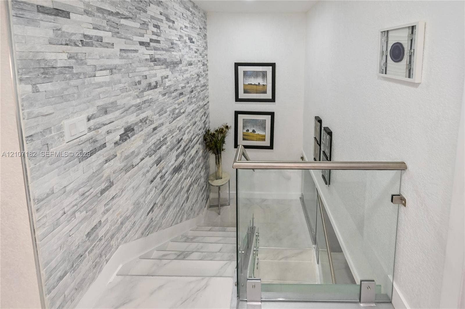 Staircase featuring stacked stone accent wall, large-format tile flooring, and glass panel railing with a metallic handrail
