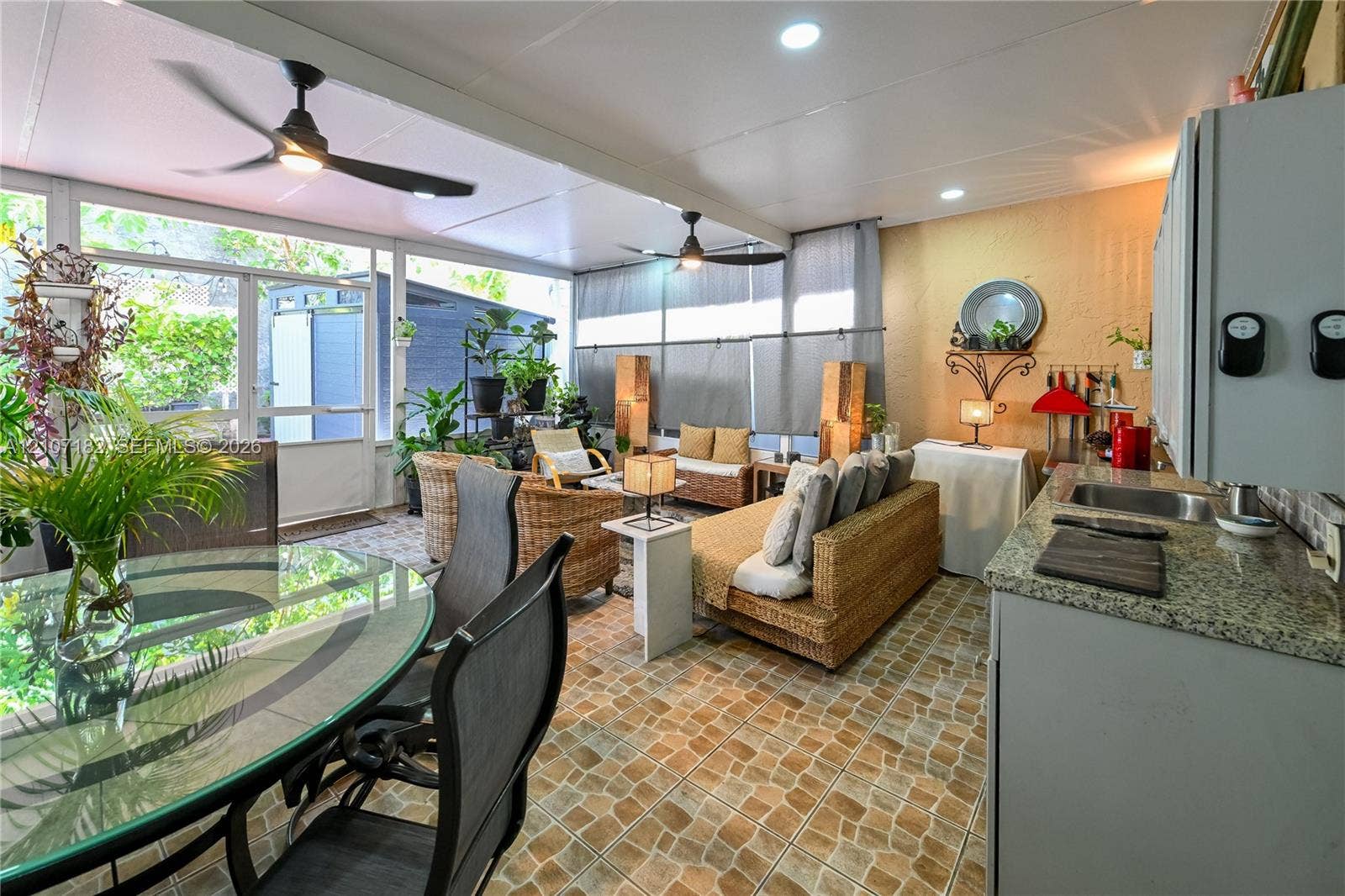 Enclosed porch featuring stone-patterned tile flooring, a stone-finish countertop with a drop-in sink, multiple recessed light fixtures, and dual ceiling fans