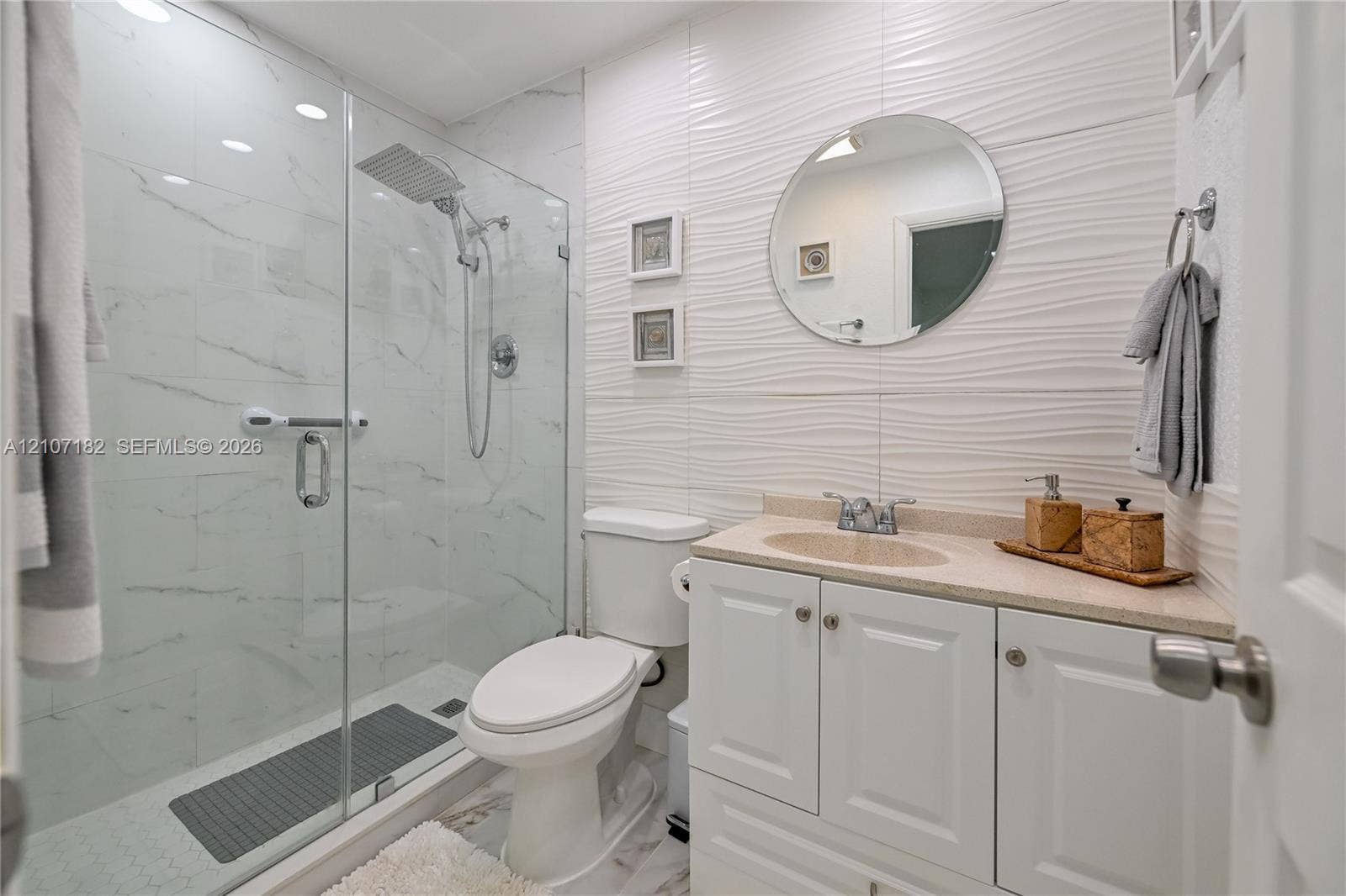 Bathroom featuring a glass-enclosed shower with rainfall showerhead, white vanity with integrated basin, stone-surface countertop, and textured wall tile