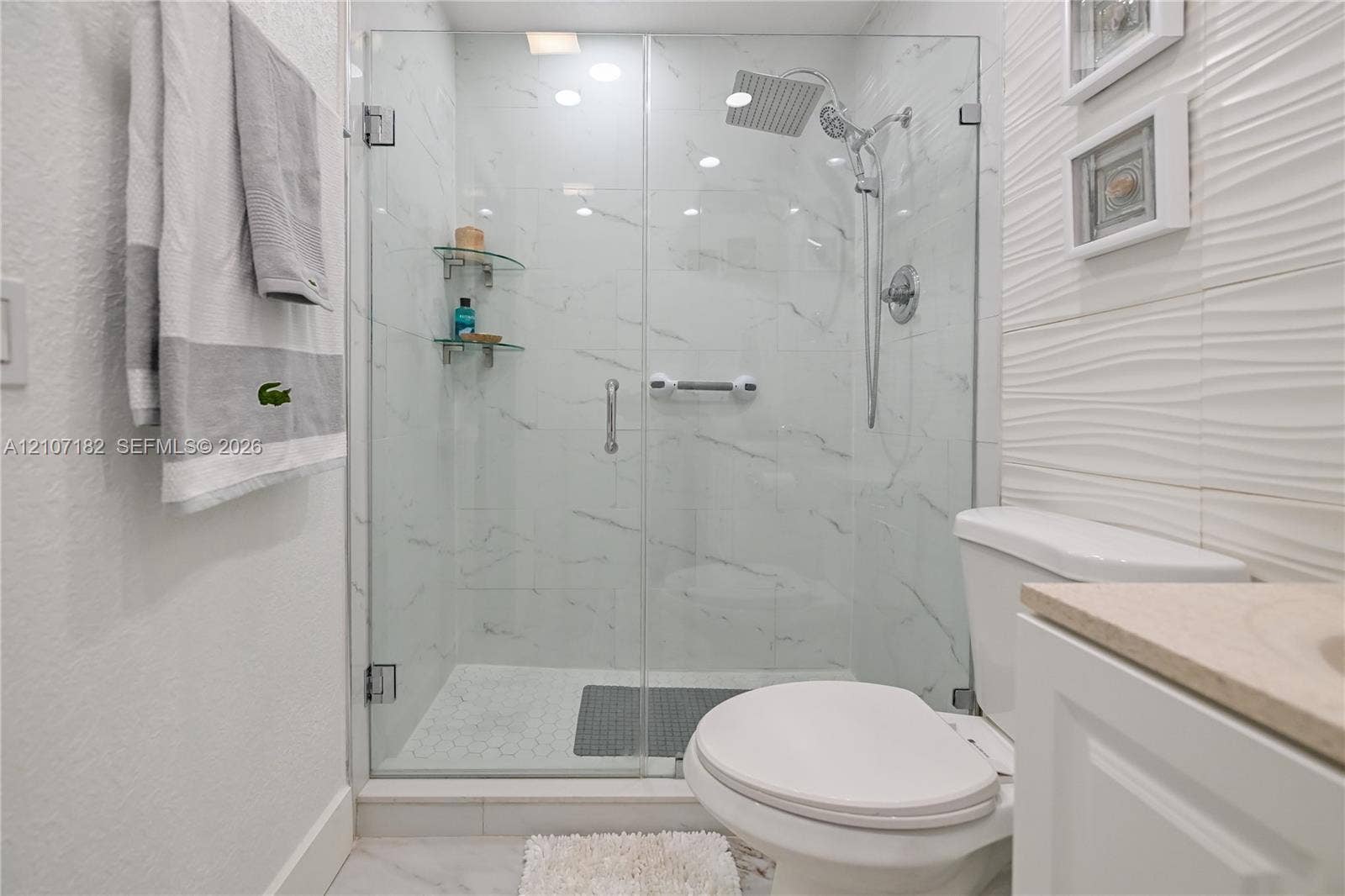 Walk-in glass-enclosed shower featuring large-format wall tile, a rain-style showerhead with a handheld attachment, and built-in glass corner shelving