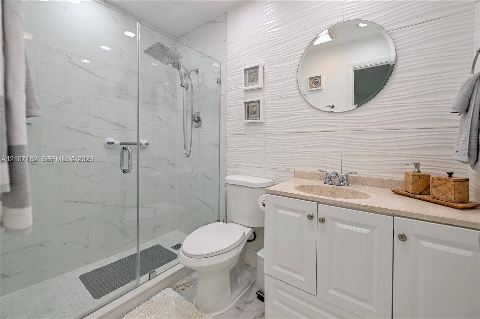 Bathroom featuring a glass-enclosed shower with a rainfall showerhead, white vanity cabinet, solid-surface countertop with an integrated sink, and textured wall tile