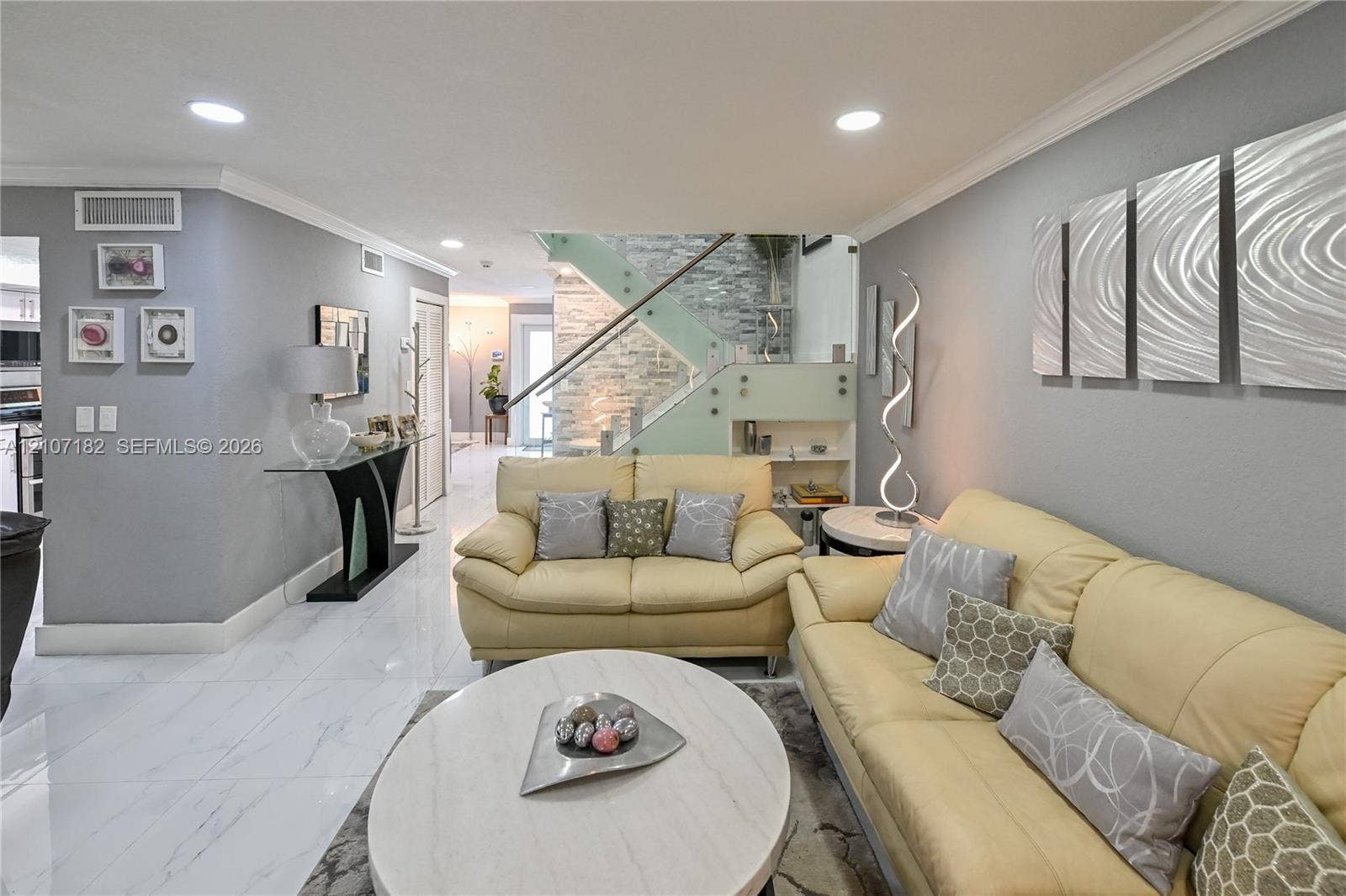 Large-format polished tile flooring, staircase featuring glass panel railings, and floor-to-ceiling stone accent wall