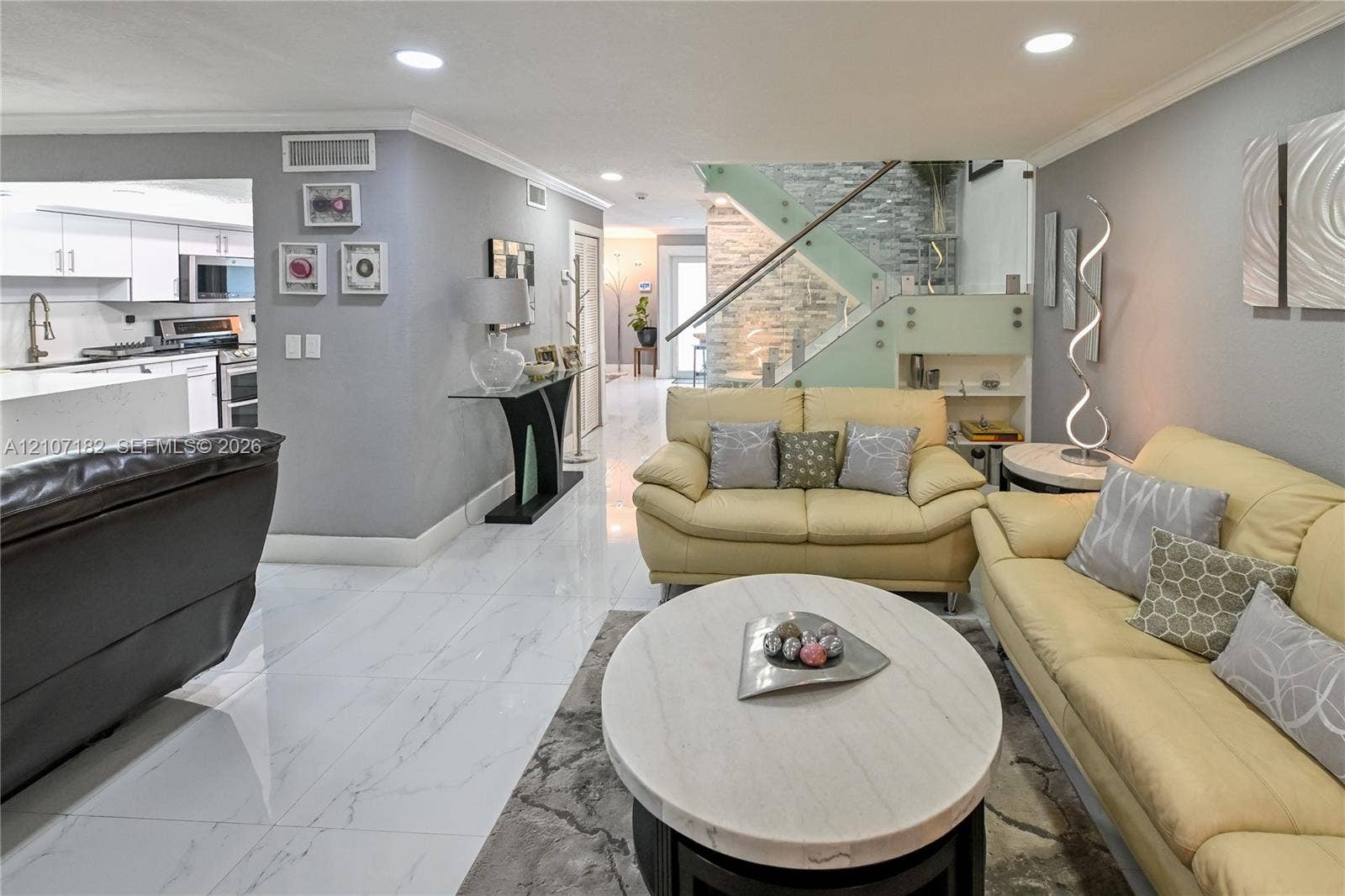 Open-concept area featuring white tile flooring, recessed lighting, and a staircase with glass panels and stone-veneer accent wall