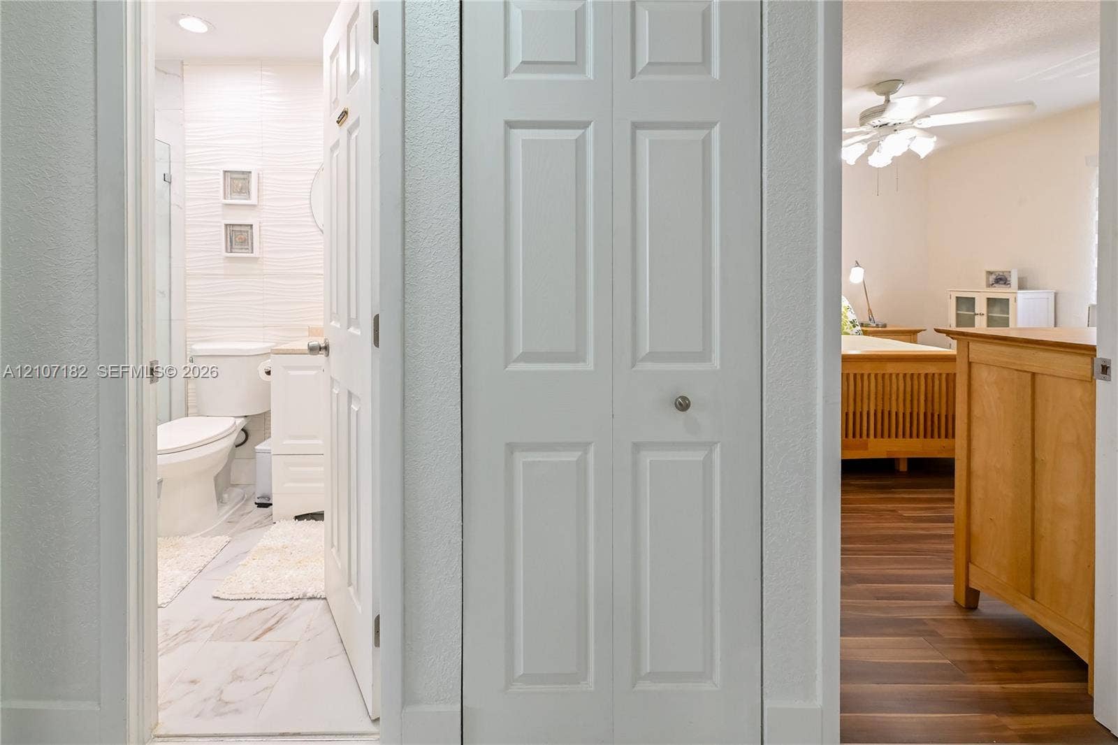 Bathroom featuring white textured wall tile, porcelain flooring, and a pedestal vanity, complemented by a hallway bifold closet and wood-finish flooring