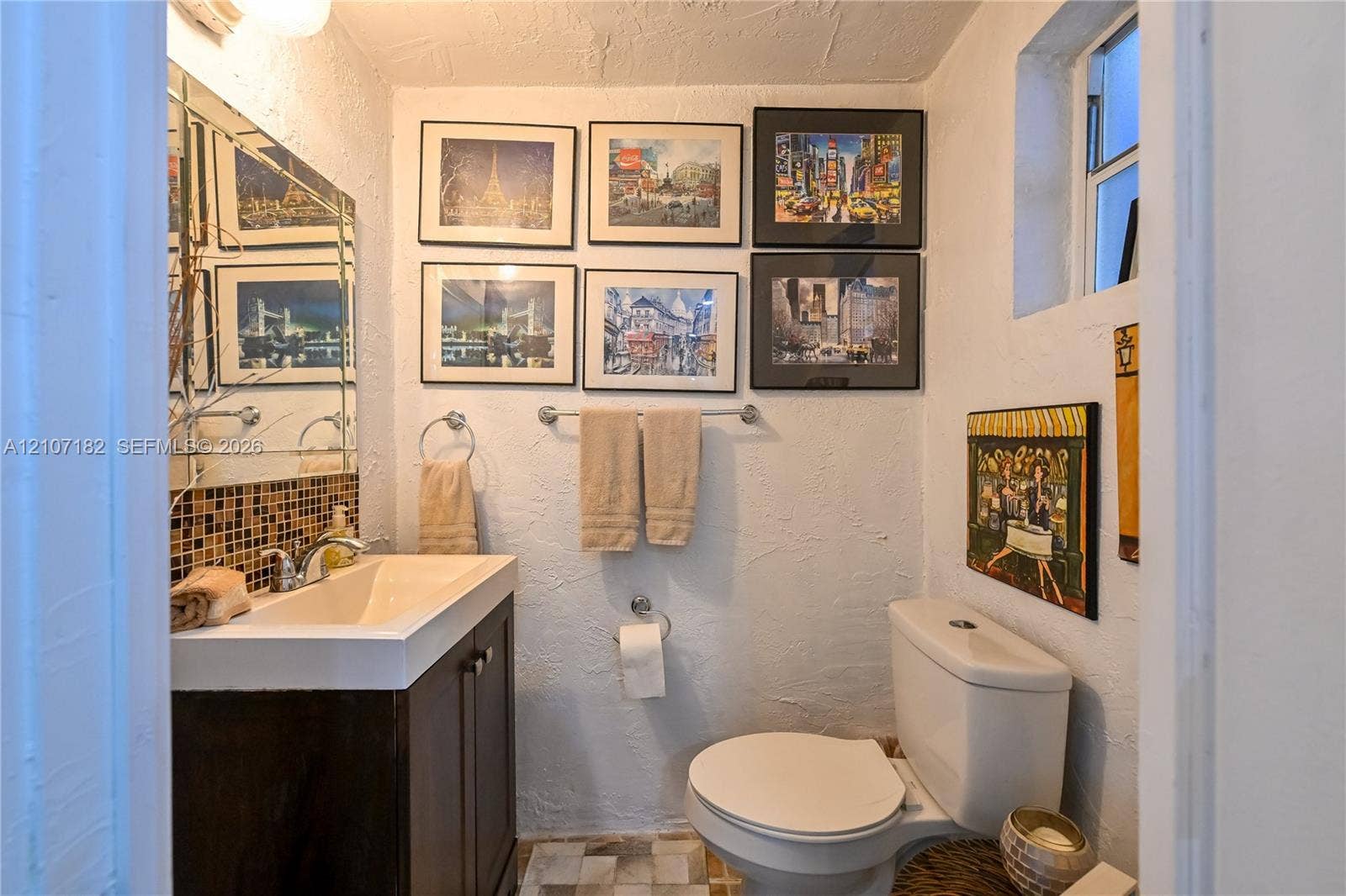 Bathroom featuring a vanity with an integrated sink, polished chrome faucet, mosaic tile backsplash, textured wall finish, and a large mirror with a decorative border