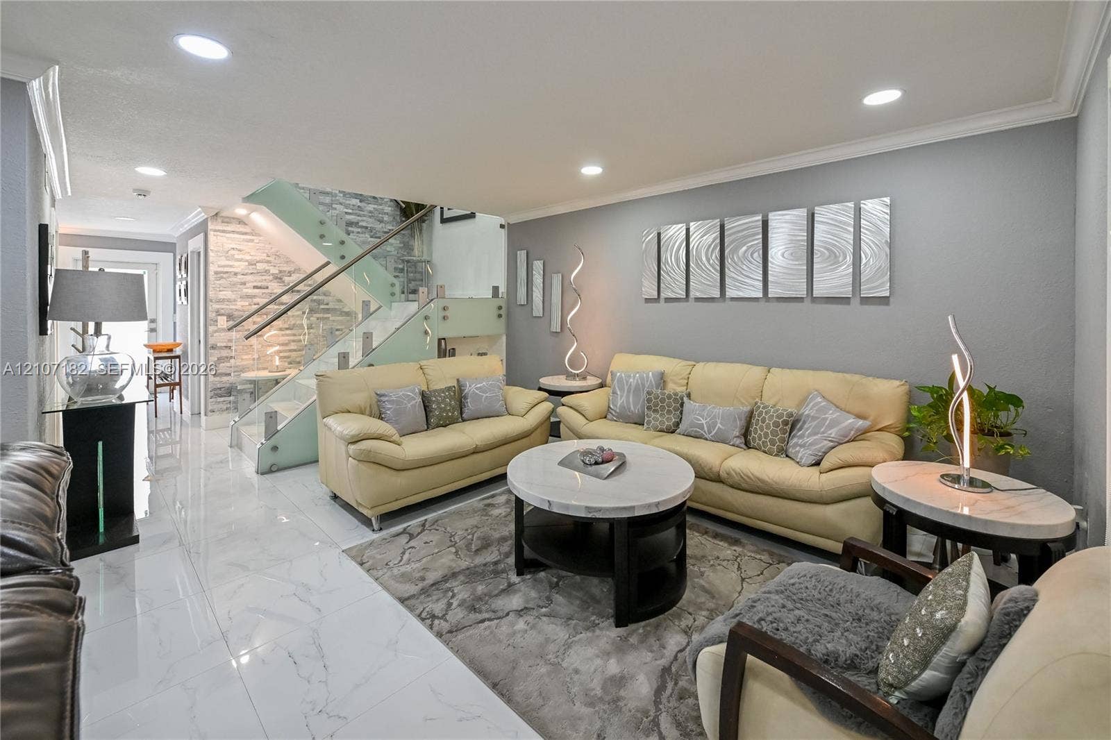 Polished porcelain tile flooring, recessed ceiling lighting, and a staircase featuring glass panels with metal railings and a textured stone accent wall