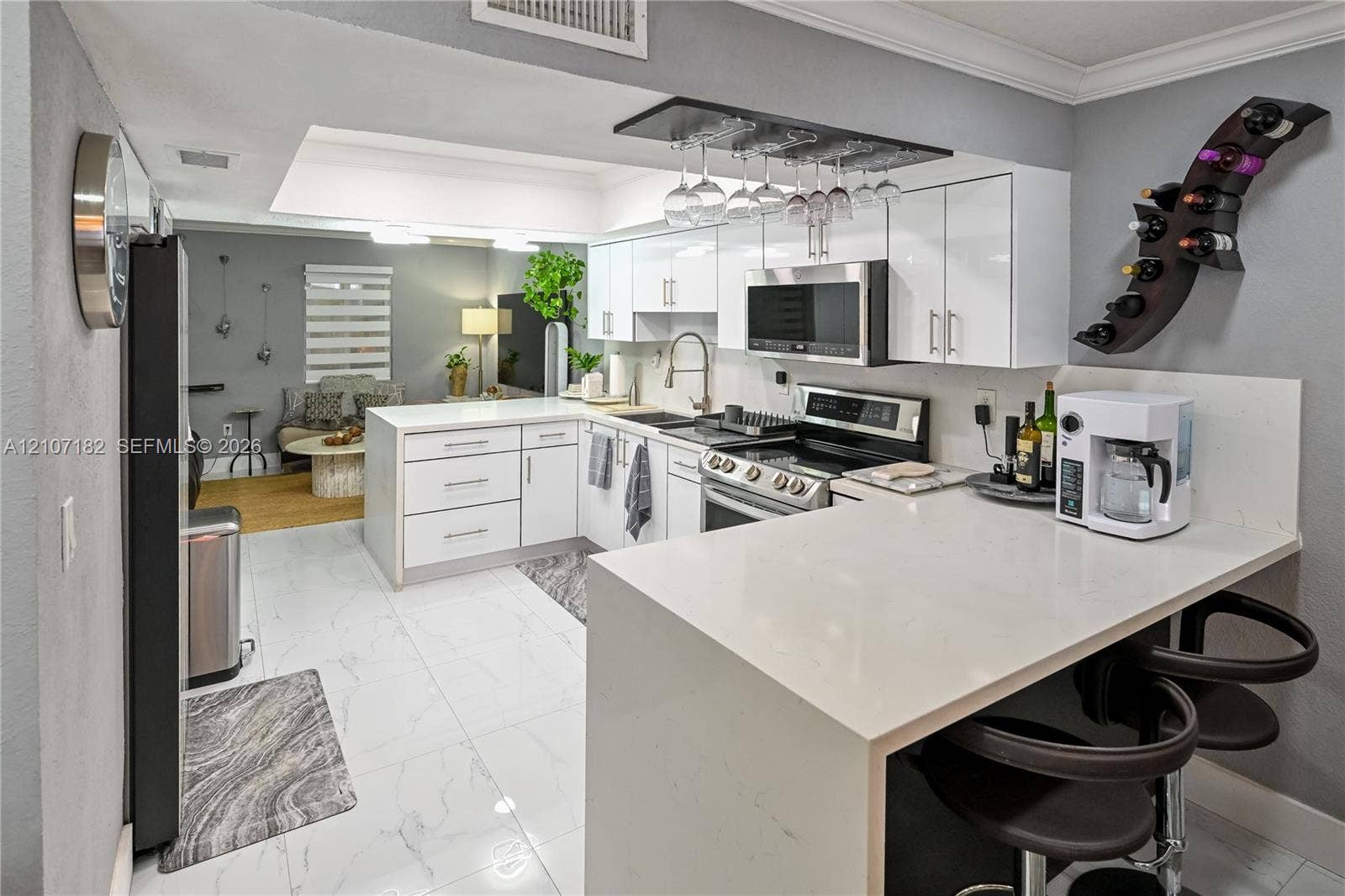 Kitchen featuring white high-gloss cabinetry, quartz countertops, a peninsula with breakfast bar seating, stainless steel appliances, and large-format tile flooring
