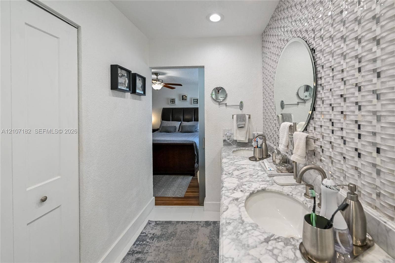 Dual-sink vanity with patterned stone countertop, custom mosaic tile backsplash, recessed lighting, and oval wall-mounted mirrors
