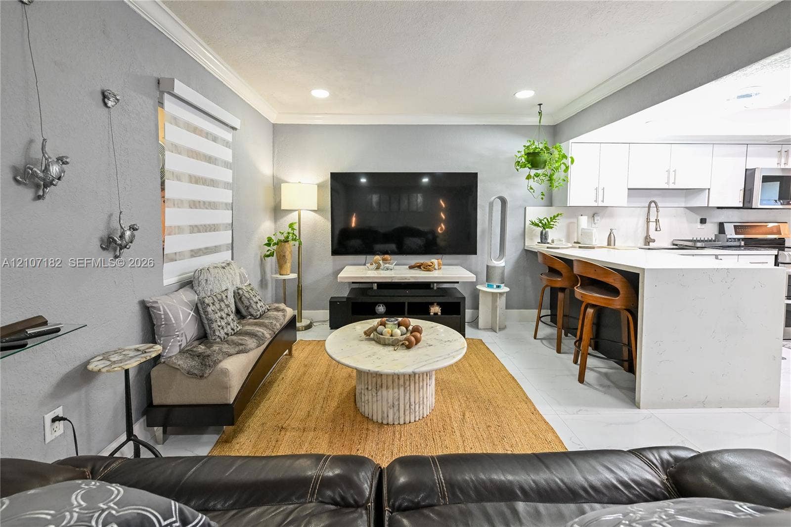 Open-concept area featuring recessed ceiling lighting, crown molding, white shaker-style cabinetry, a stone-finish waterfall edge kitchen island, and tile flooring