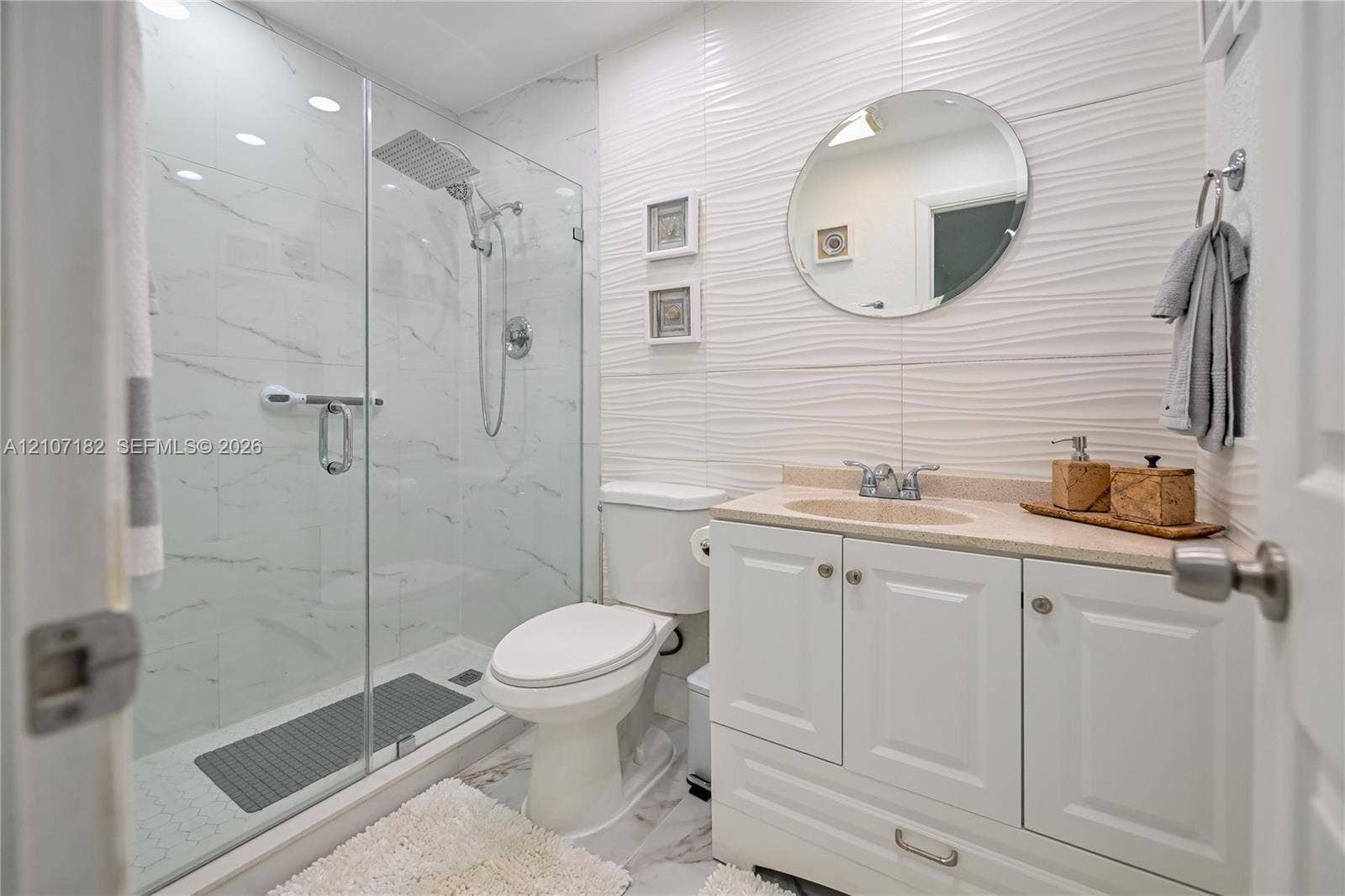 Walk-in shower with floor-to-ceiling stone-patterned tile and rainfall showerhead, white vanity with integrated countertop, and textured accent wall tiling