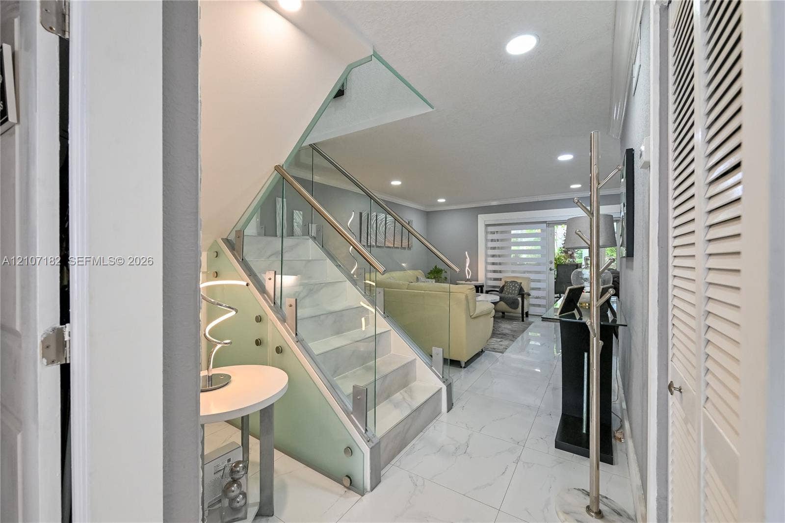 Staircase featuring white stone-finish steps, glass balustrade, and stainless steel handrail, complemented by large-format white tile flooring and recessed ceiling lighting