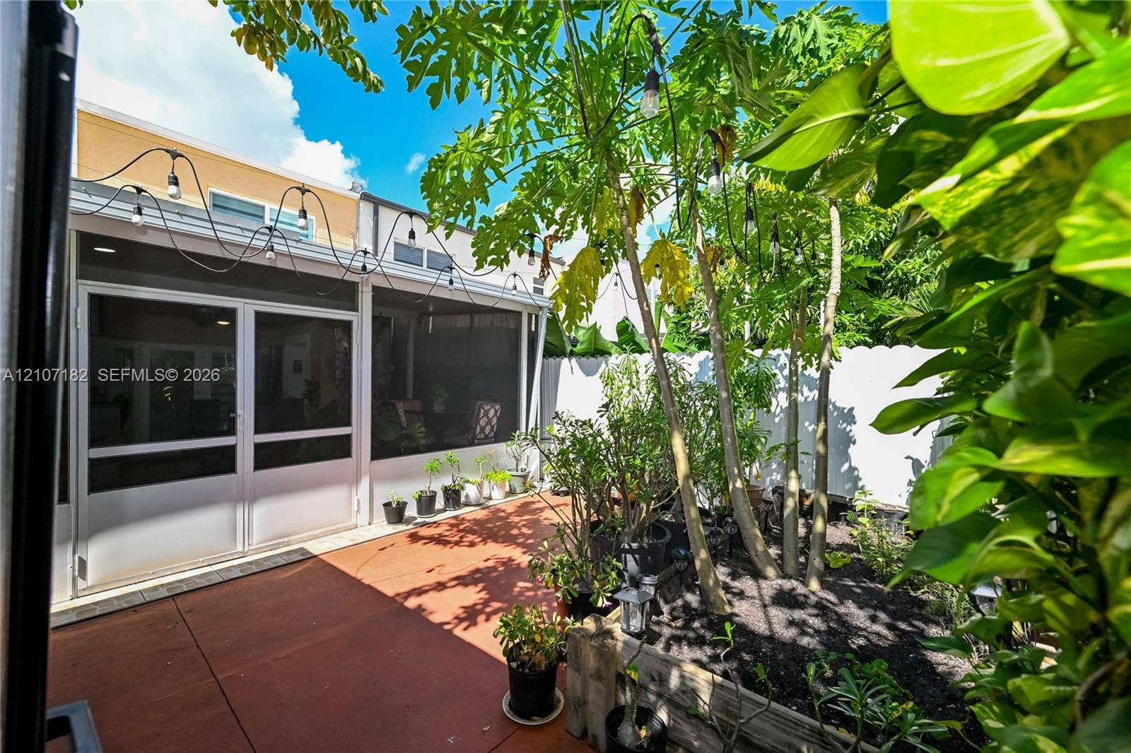 Screened-in patio with tiled flooring, raised garden beds, and white privacy fencing