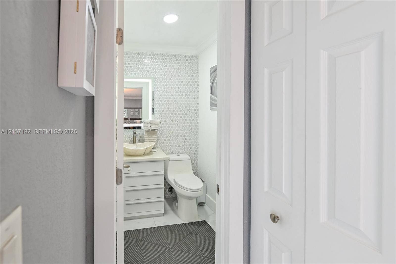 Bathroom featuring a white vanity cabinet with a vessel sink, geometric mosaic tile wall, one-piece dual-flush toilet, and diamond-patterned floor tile