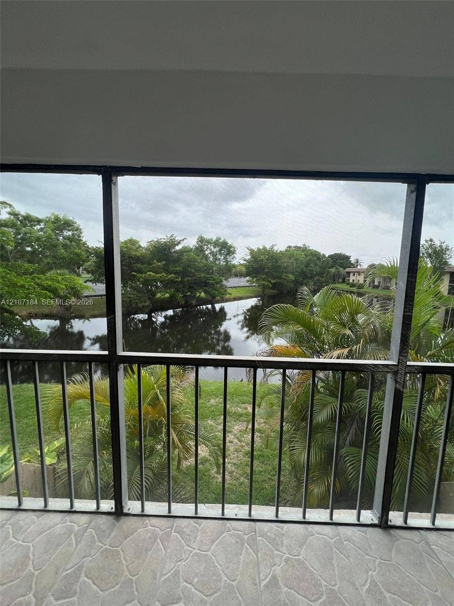240 Lakeview Drive, #209, Weston, Weston, FL 33326 Screened-in balcony featuring stone-finish tile flooring, metal railing, and direct exposure to a water feature with surrounding mature landscaping