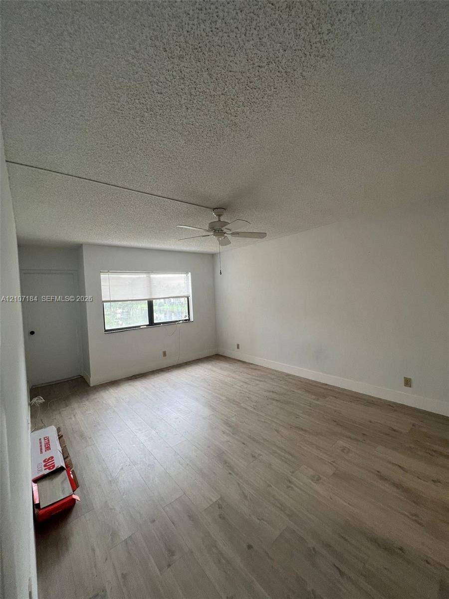 240 Lakeview Drive, #209, Weston, Weston, FL 33326 Room featuring wood-finish flooring, a textured ceiling, a central ceiling fan with integrated lighting, and a window with a roller shade
