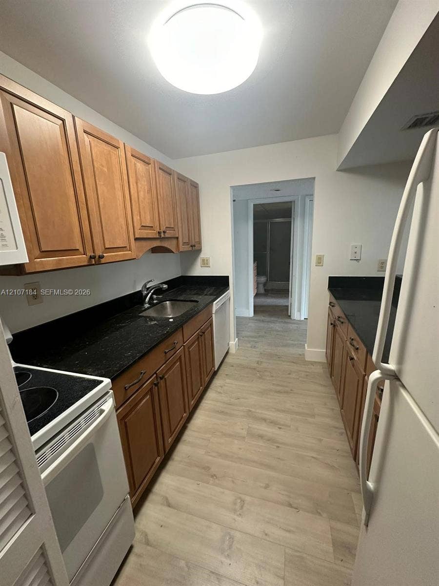 240 Lakeview Drive, #209, Weston, Weston, FL 33326 Kitchen featuring wood cabinetry, dark stone-finish countertops, stainless steel sink with metal faucet, and wood-finish flooring