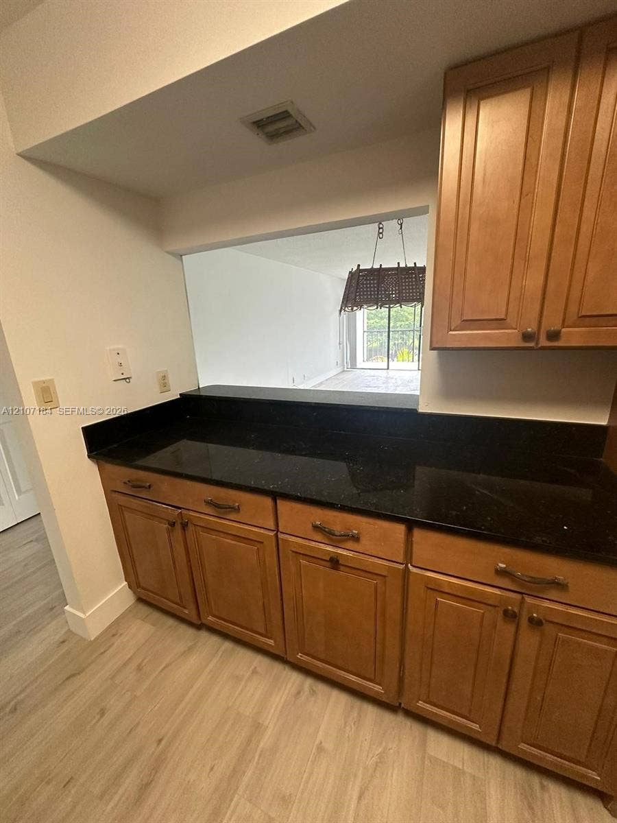 240 Lakeview Drive, #209, Weston, Weston, FL 33326 Kitchen cabinetry with shaker-style doors, black stone countertop, pass-through window, and wood-finish flooring