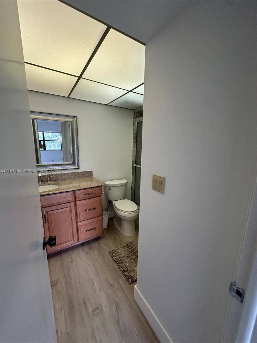 240 Lakeview Drive, #209, Weston, Weston, FL 33326 Bathroom featuring wood-finish flooring, a wood vanity with a solid surface countertop, an integrated sink, and an enclosed shower stall